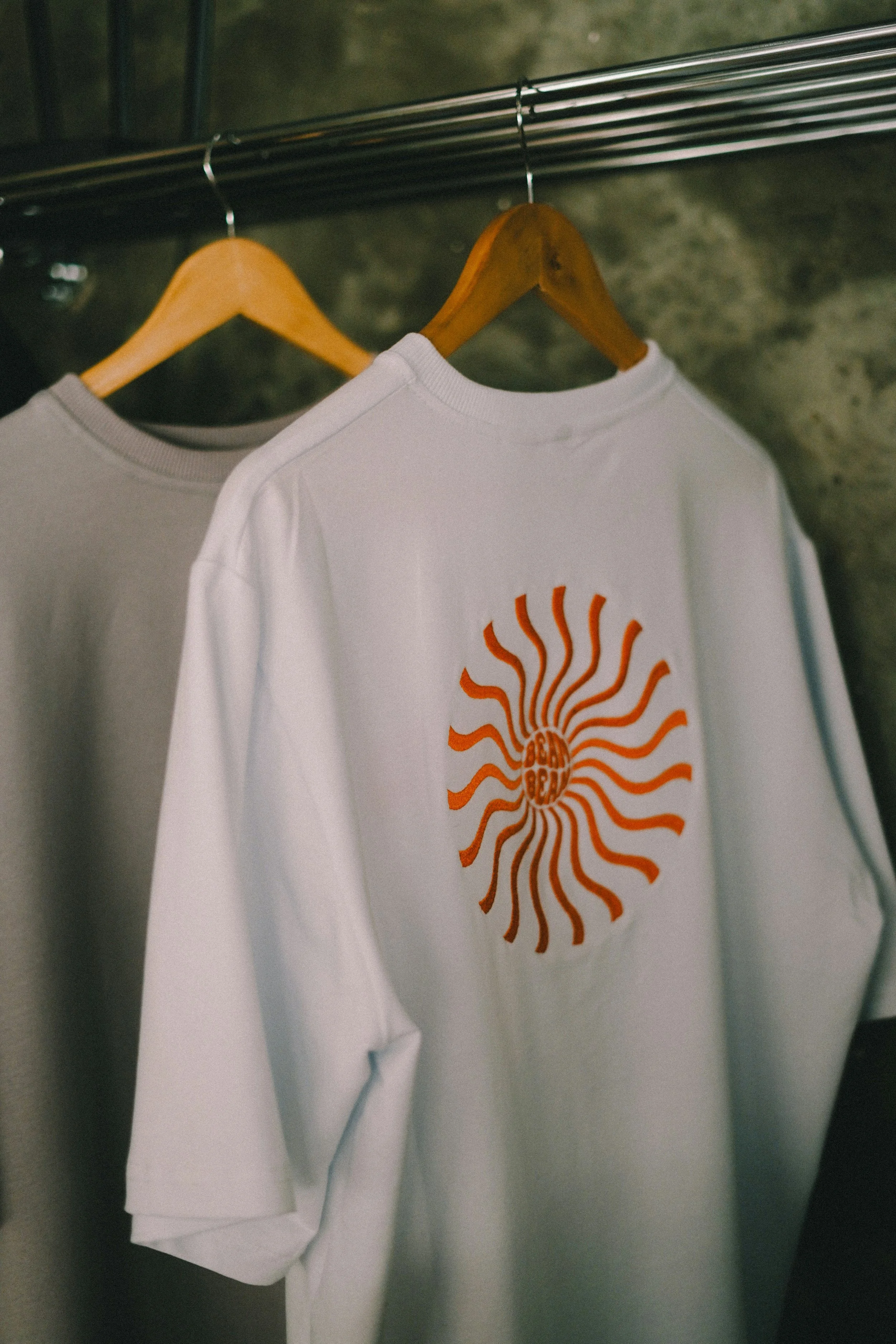 White T-shirt with an orange sunburst design hanging on a wooden hanger