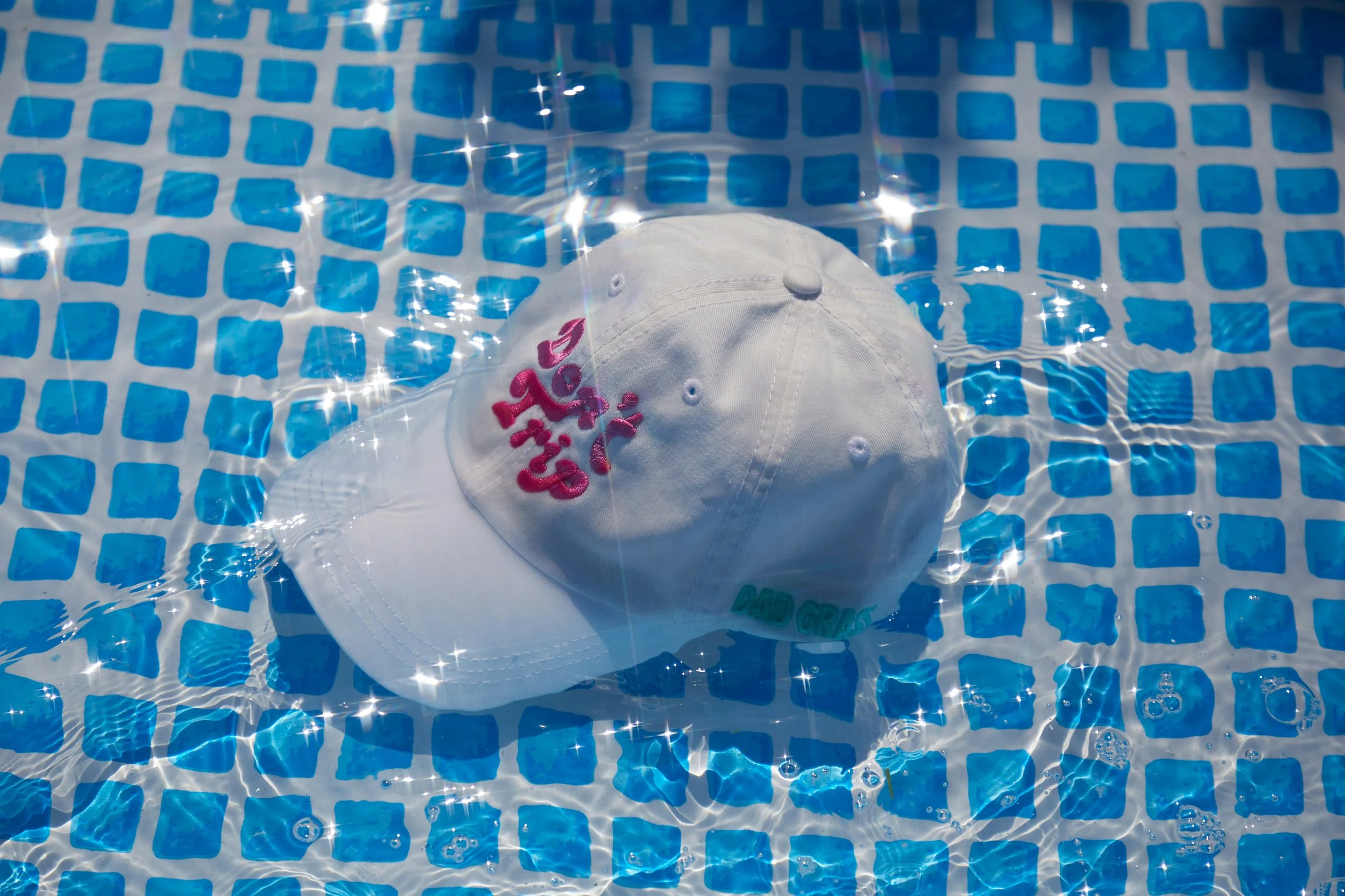 A white cap floating in a swimming pool with blue tiles, with sunlight reflecting off the water.