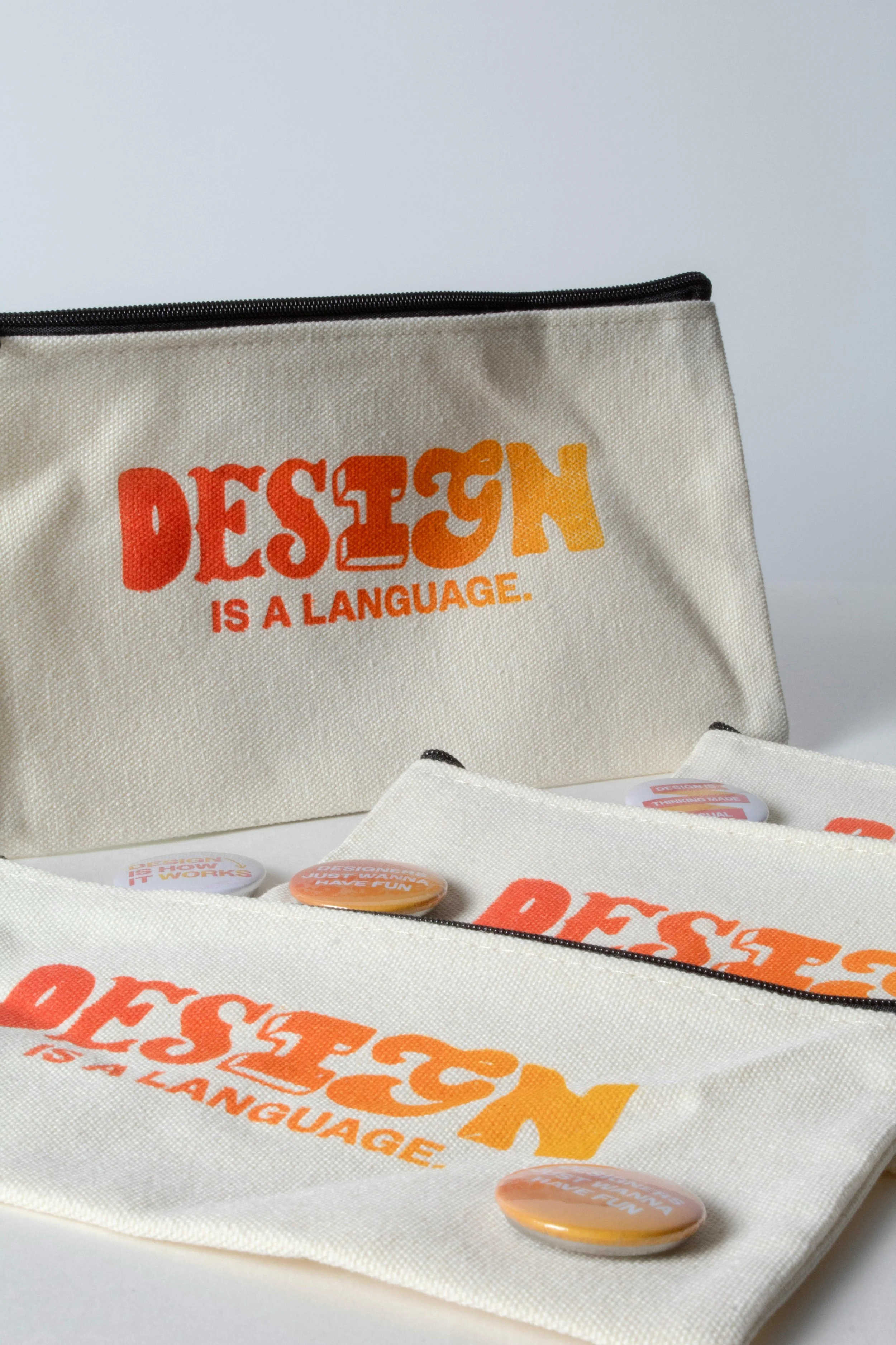 Various fabric pouches with orange text that reads 'Design is a language' and round buttons with similar phrase on a white background.