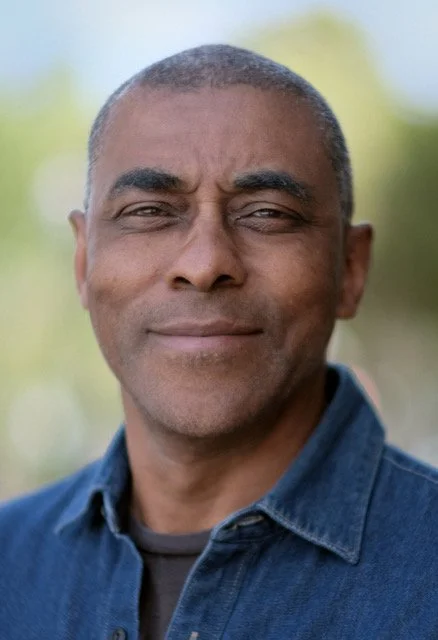 Close-up of a middle-aged man outdoors, wearing a denim jacket, with short hair and a confident expression.