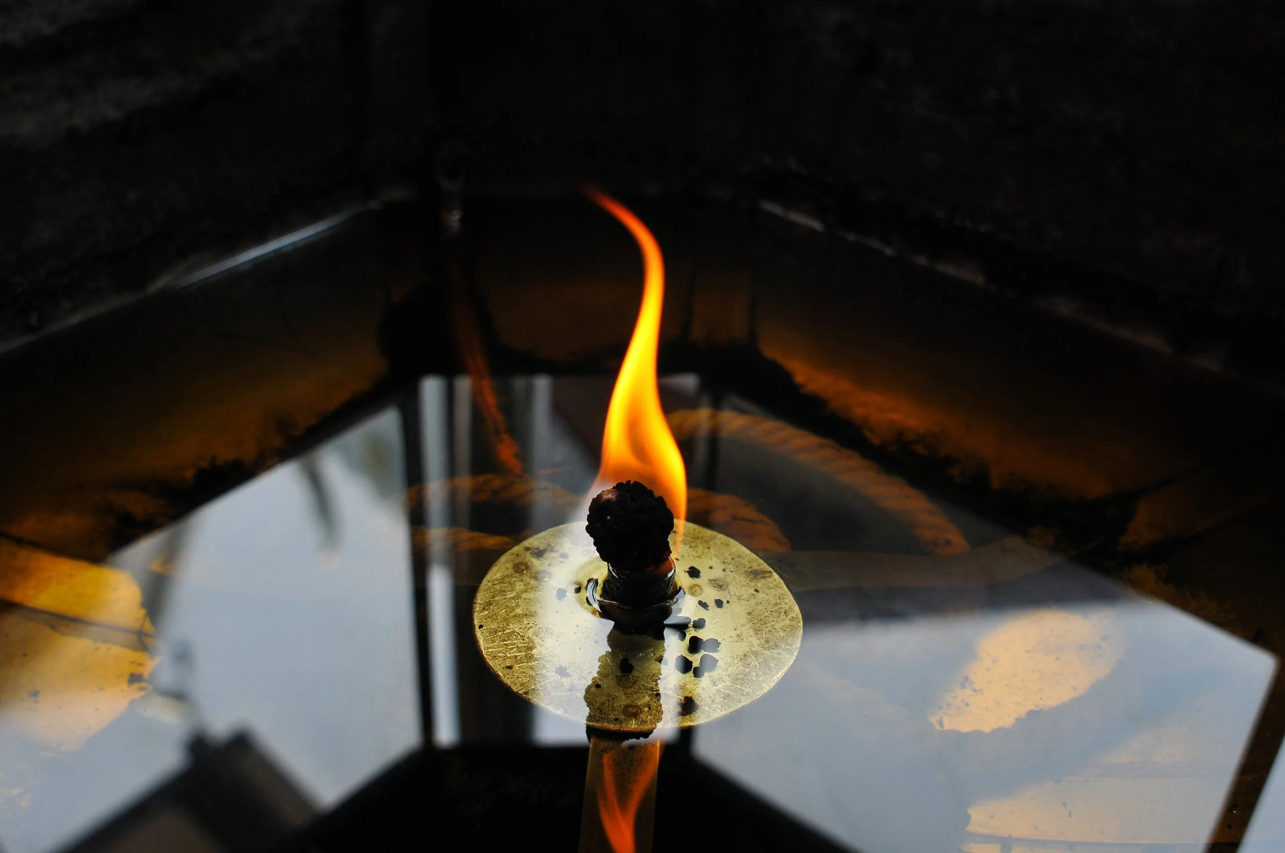 Une bougie allumée avec une flamme orange sur une surface en métal reflétant des éléments environnants