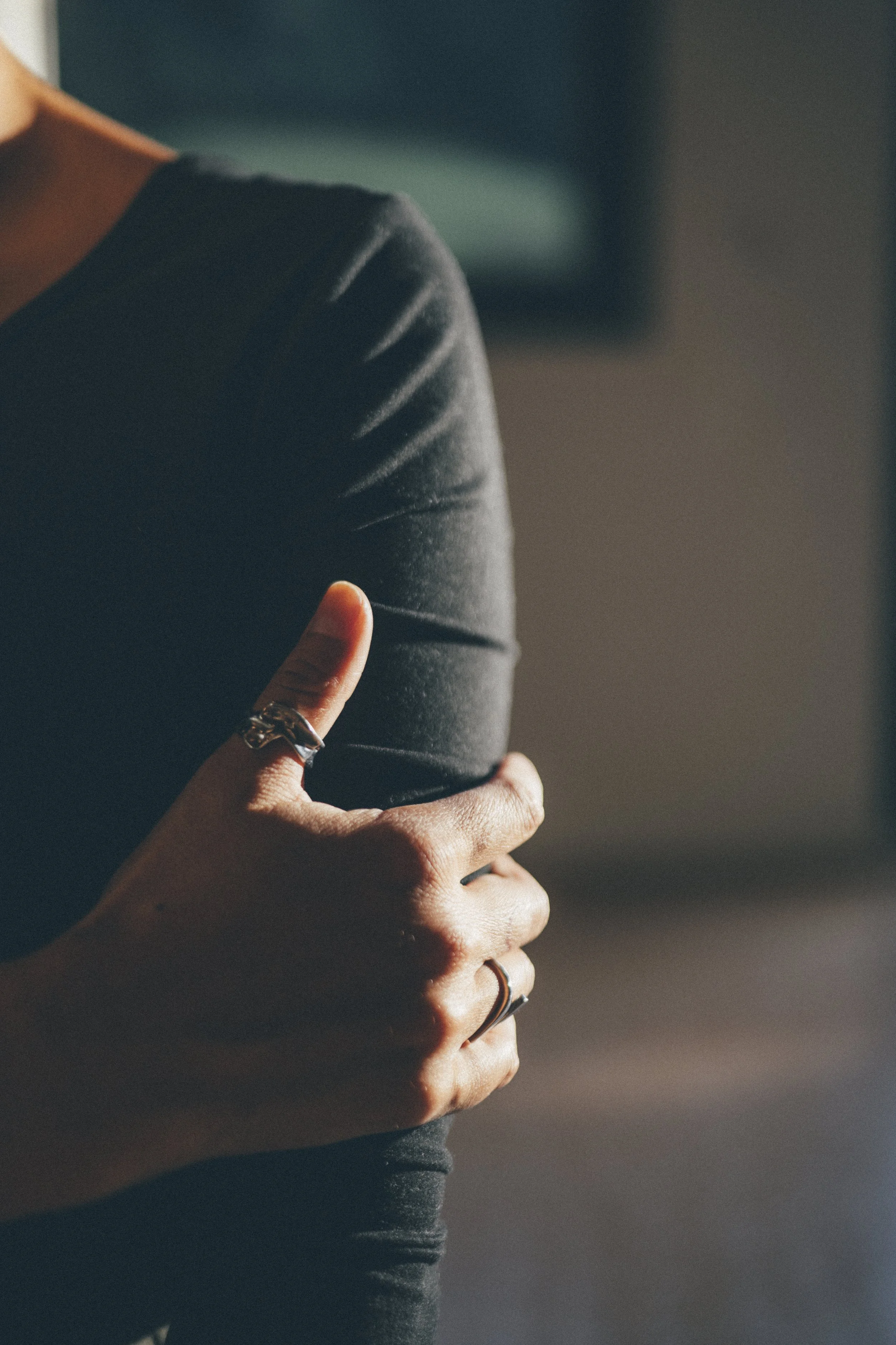 Une personne entenue par la hanche, portant des vêtements noirs, avec des bagues aux doigts, dans un éclairage tamisé.