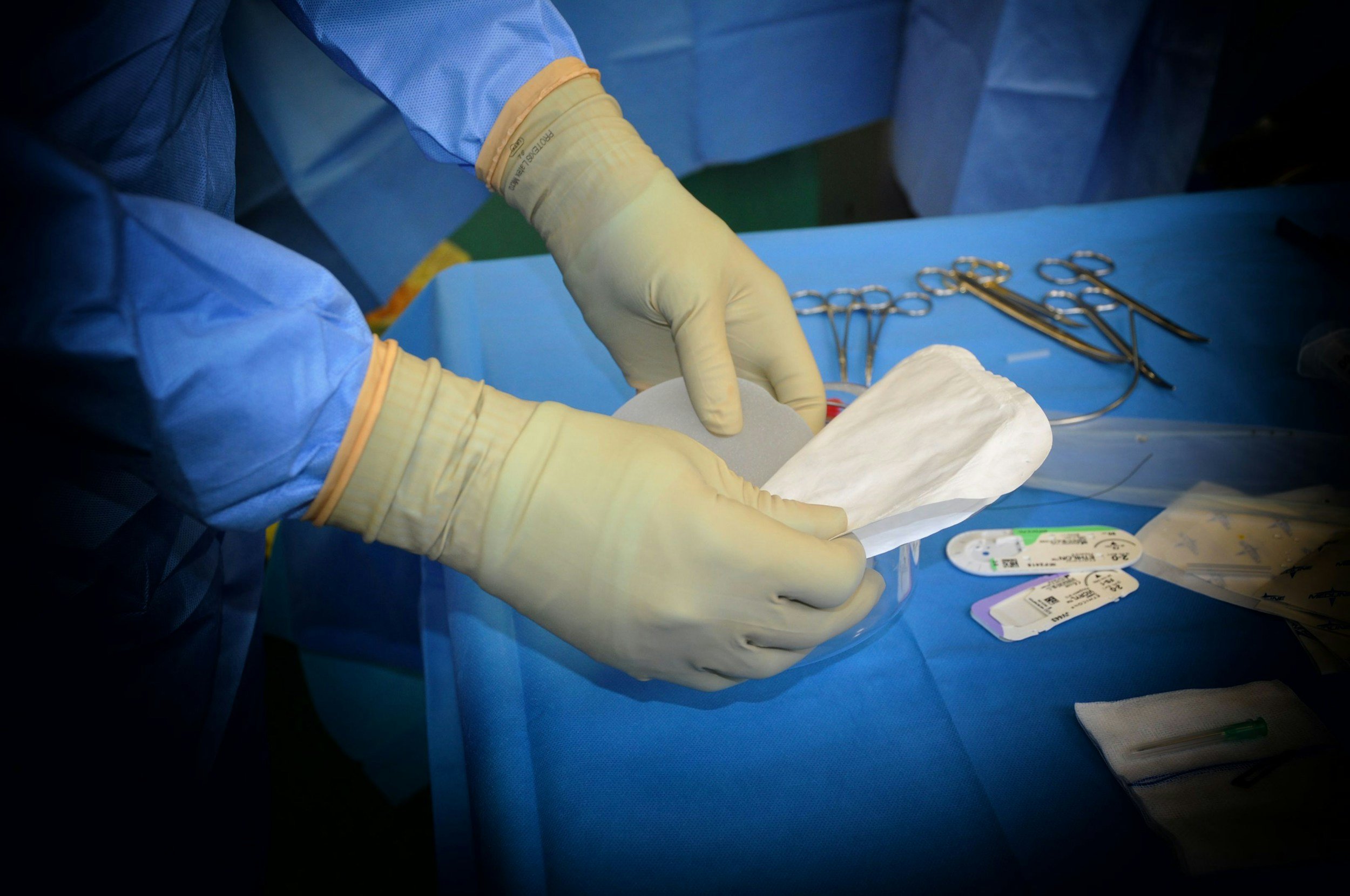 A stifle surgeon, Matthew Robinson wearing gloves and surgical gown handling medical supplies, preparing to perform a TPLO for cruciate rupture in a dog.ical tray, including sterile tools and medical labels.