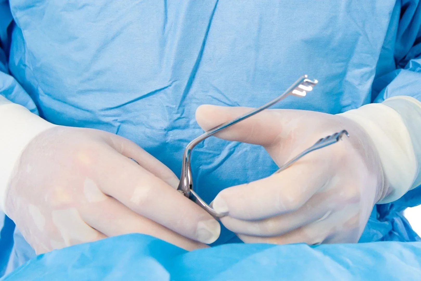 Close-up of a veterinary surgeon's hands, from Stifle Surgeons, wearing gloves, holding surgical instruments during an operation like a TPLO for cruciate rupture in a dog.