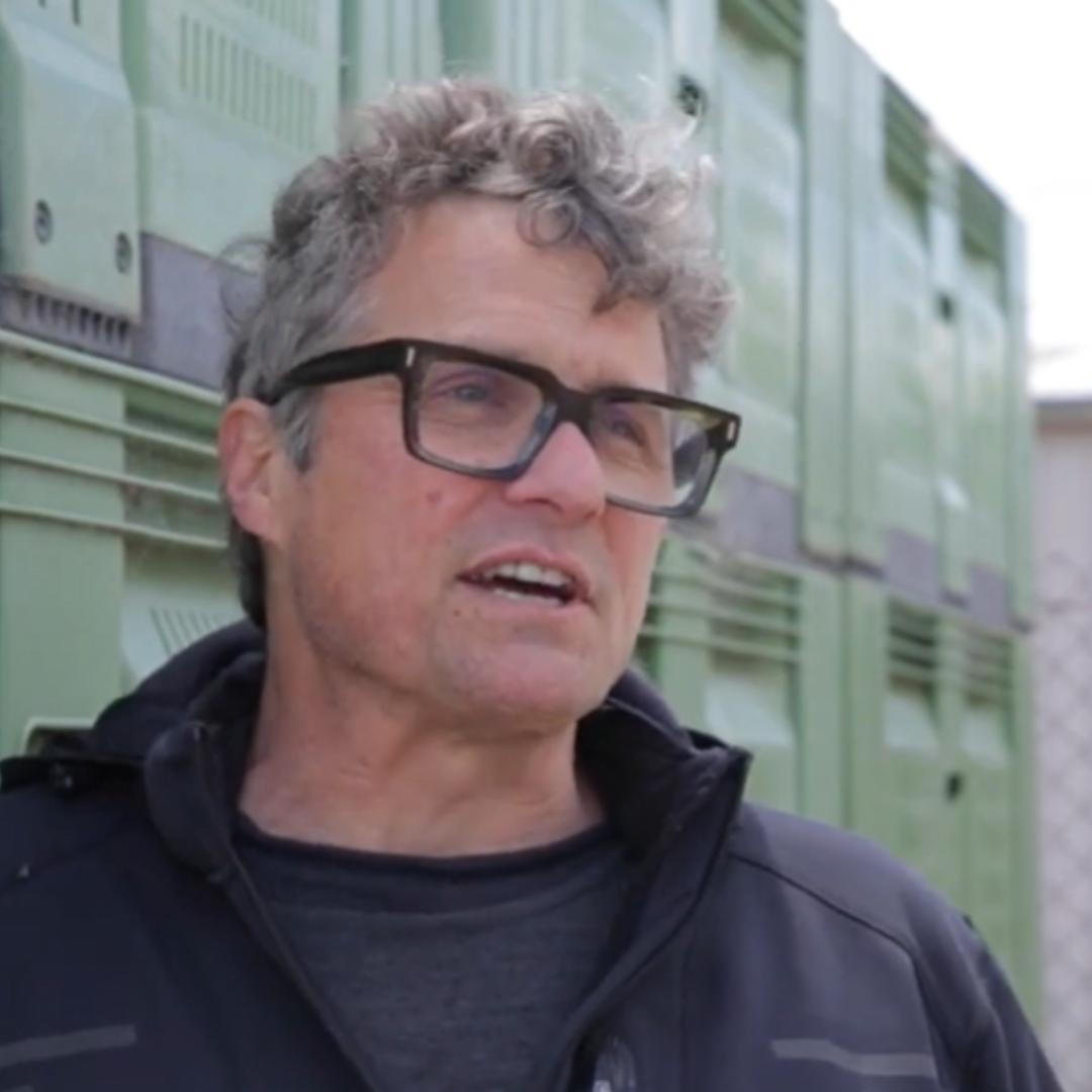 Andrew Kerekes, Chief Product Officer. A man with curly gray hair and black glasses speaking outdoors, with green lockers in the background.
