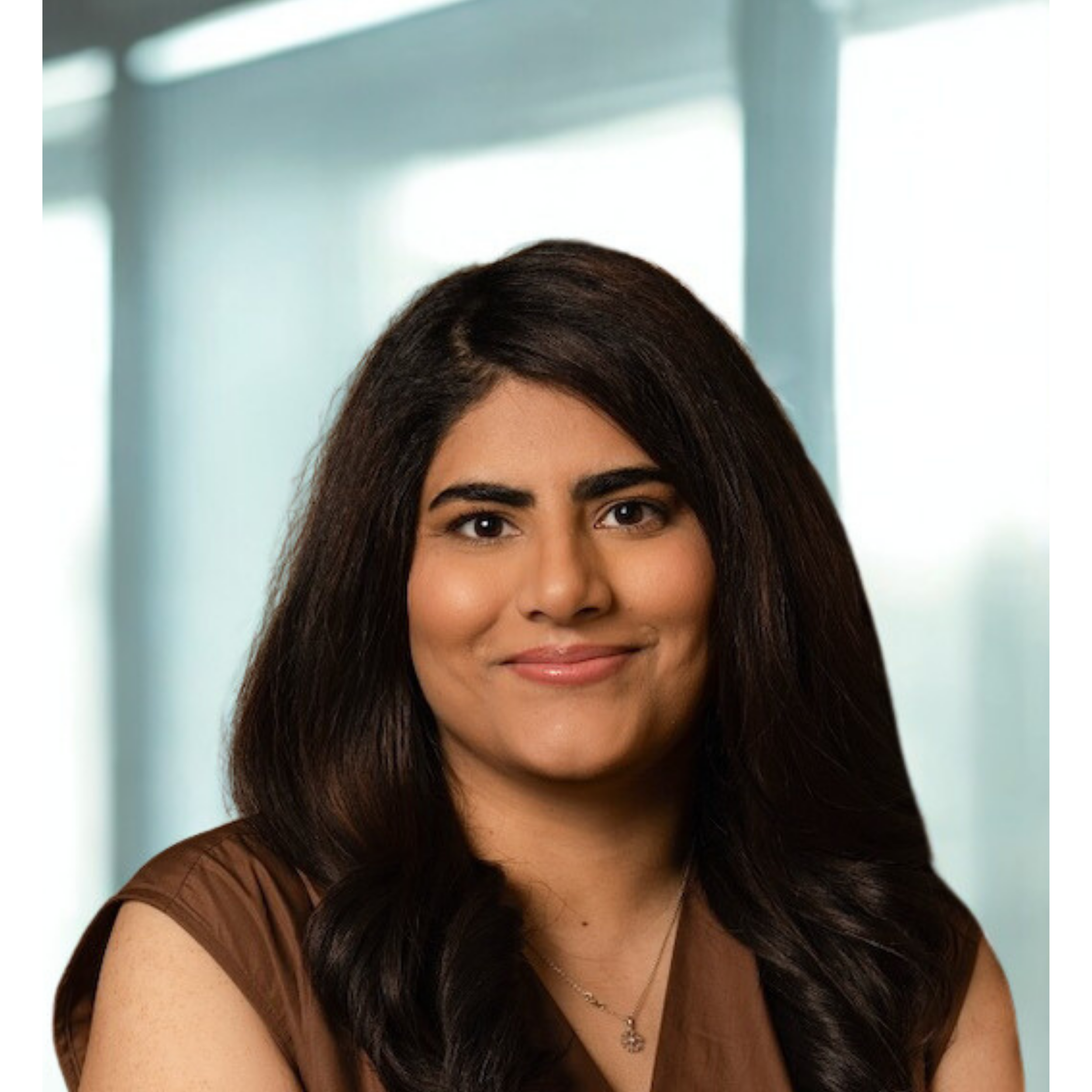 Close-up of a woman with long dark hair, smiling slightly, wearing a dark top, with a blurred background.