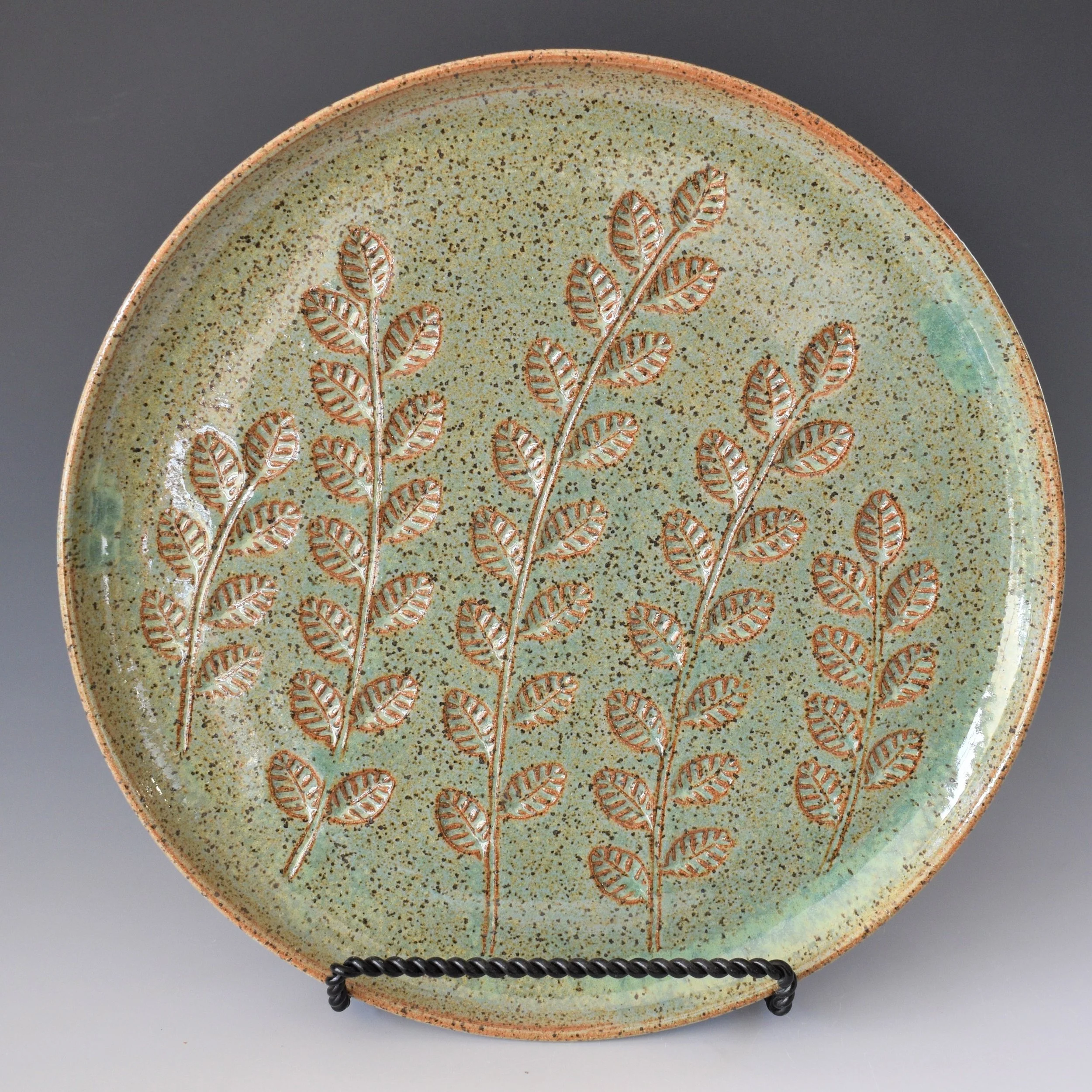 A round ceramic plate with a textured green glaze, decorated with an engraved pattern of stylized, leaf-like shapes outlined in orange.