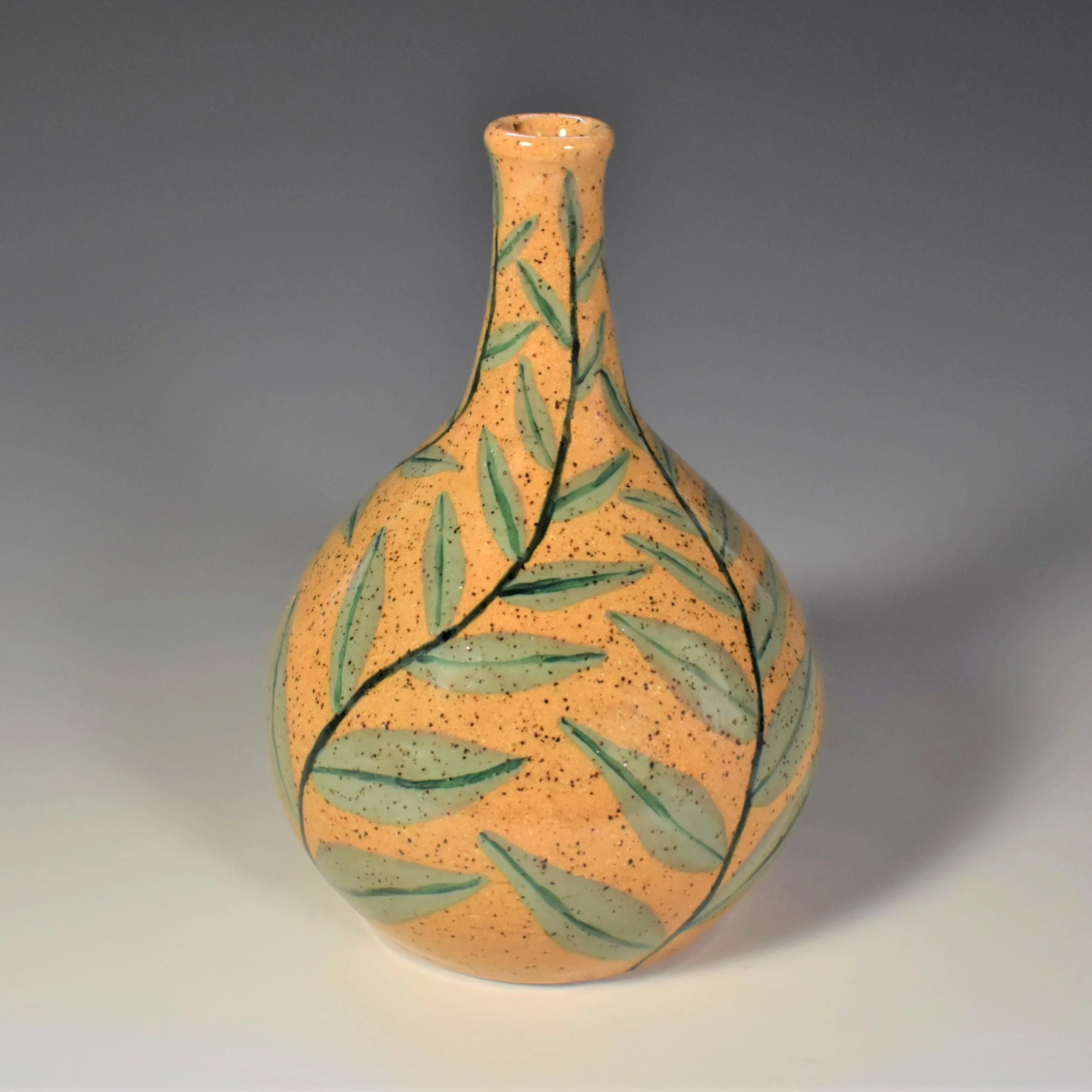 A ceramic vase with an orange speckled glaze decorated with green leaf patterns.