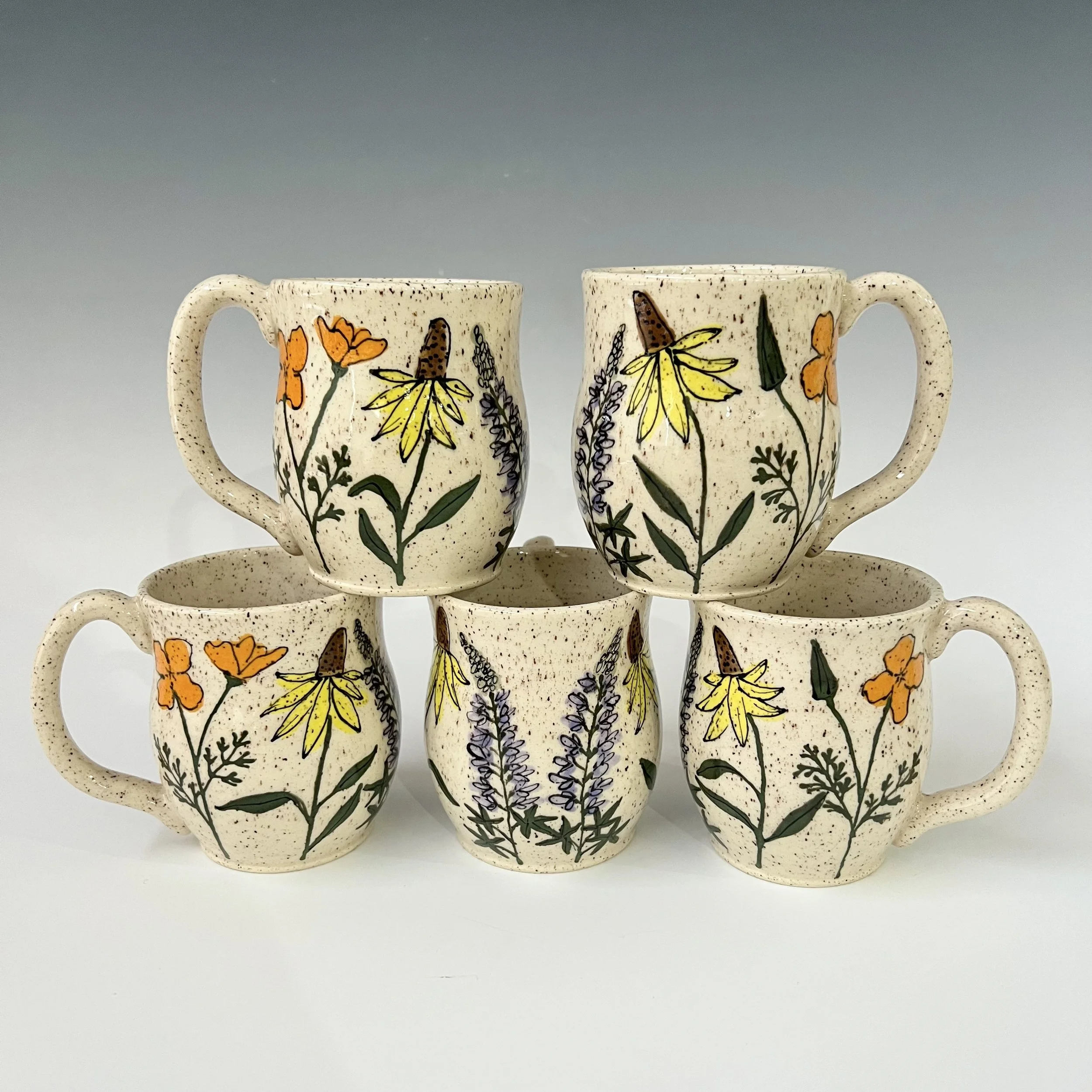 A set of cream-colored coffee mugs with speckled texture and floral illustrations featuring yellow, orange, and purple flowers, arranged on matching saucers.