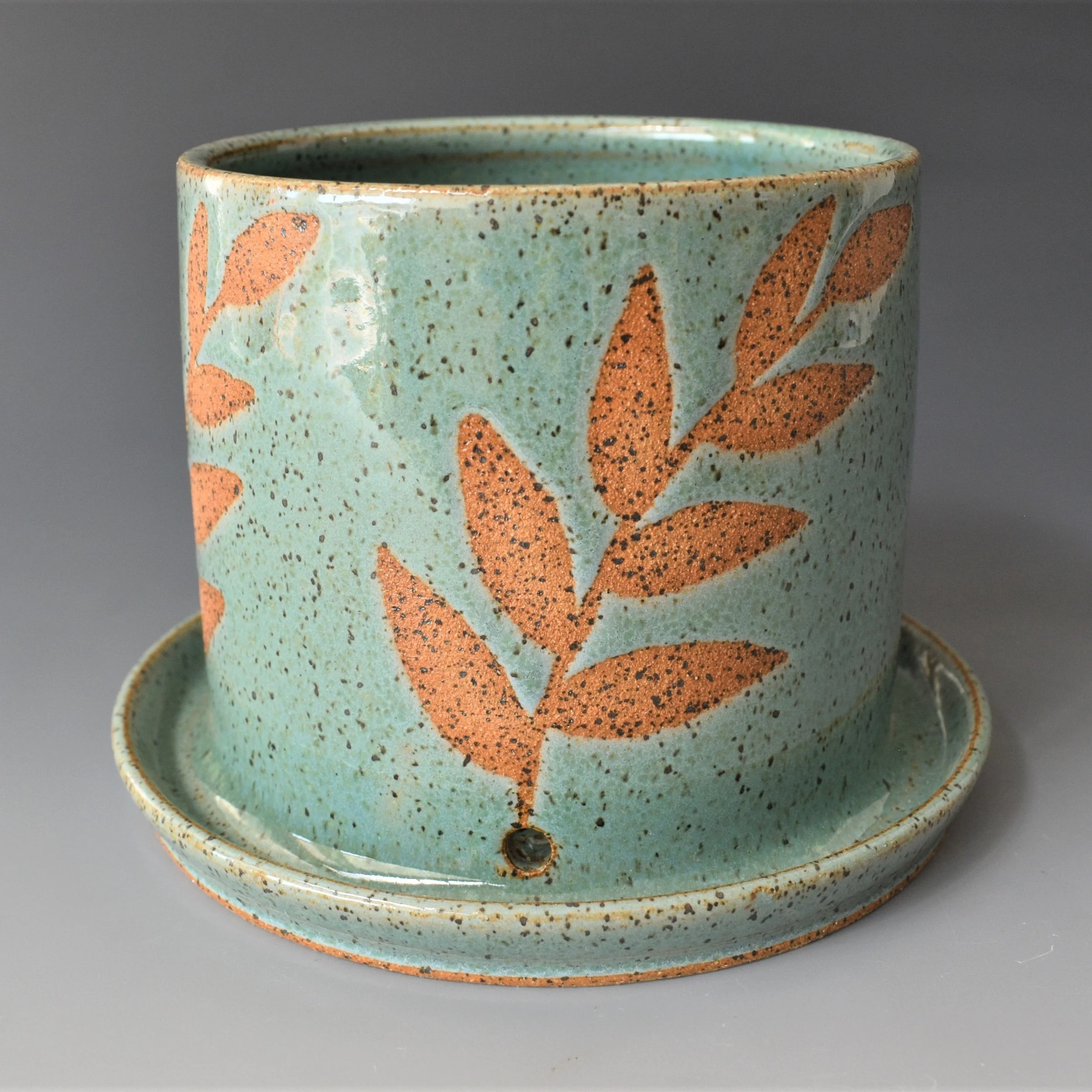 Close-up of a ceramic cup with mint green glaze and reddish-brown leaf patterns, on a gray background.
