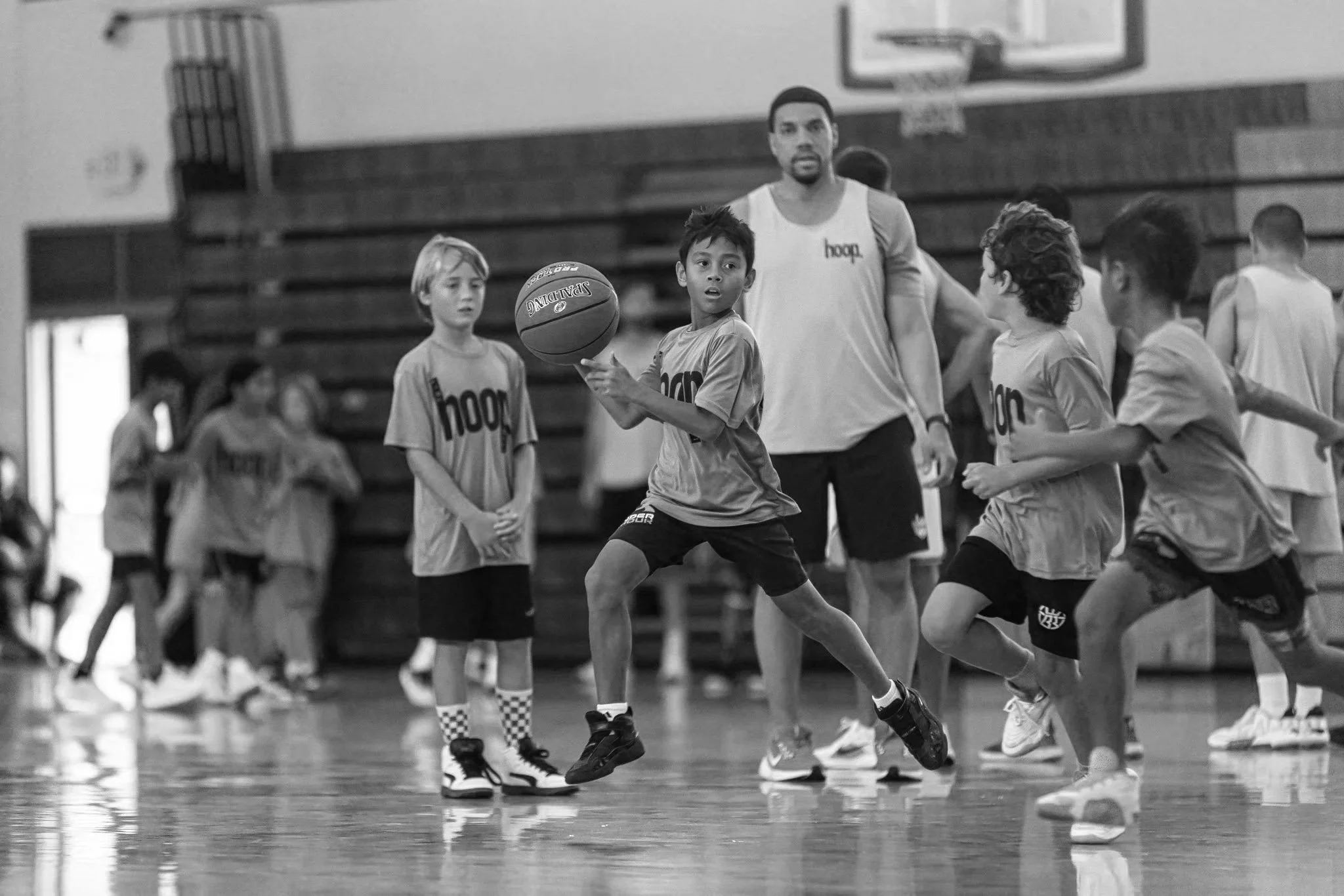 Young children playing basketball under the supervision of an adult coach in a gymnasium.
