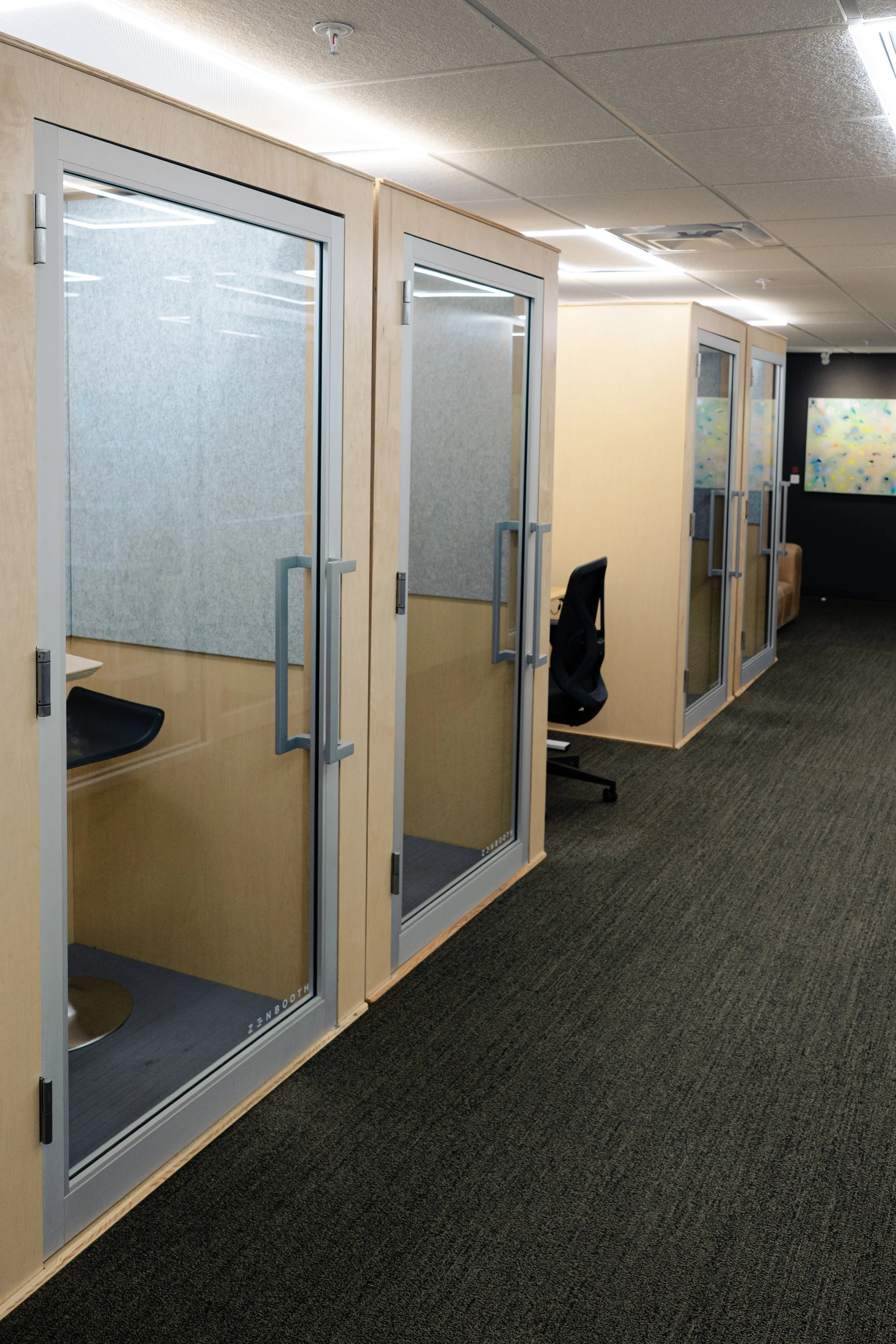 Office cubicles with glass doors, chairs, and a artwork on the wall.
