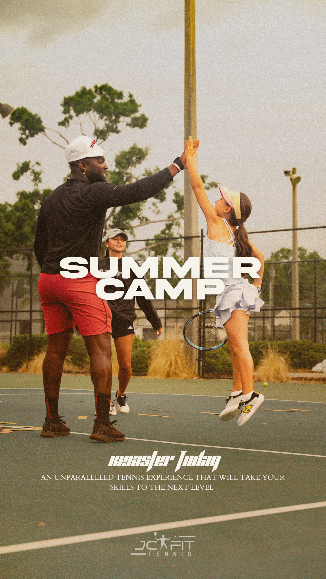A man high-fiving a young girl on a tennis court during summer camp, with another girl in the background, all in athletic clothing and tennis gear.