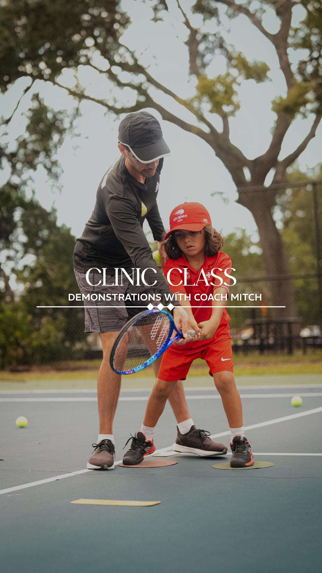 A coach demonstrates tennis techniques with a young child on a tennis court, surrounded by tennis balls and trees.