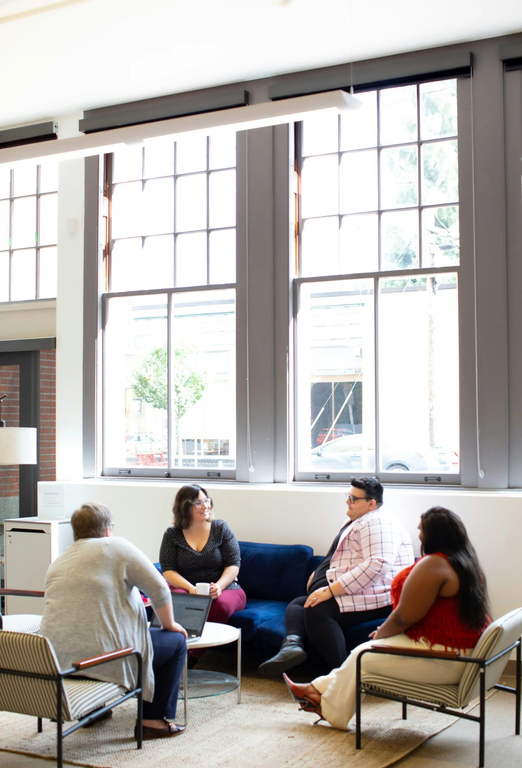 Four people sitting and talking in a brightly lit room with large windows and a blue sofa.