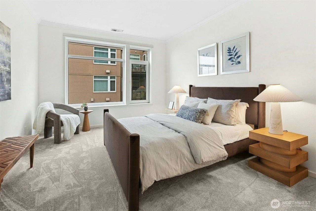 Staged primary bedroom with wood bed frame and reading chair in a Seattle waterfront condo