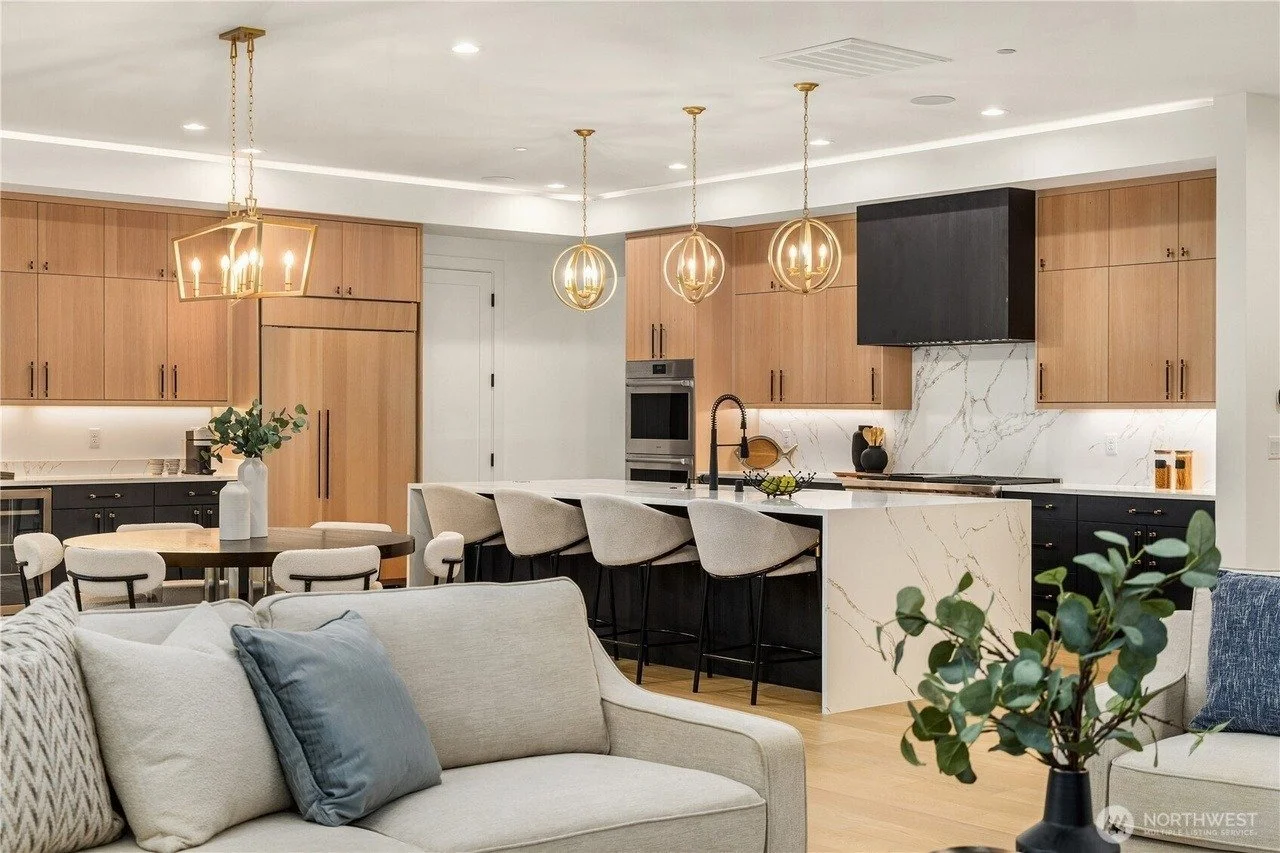 Staged great room with sofa facing an open kitchen with gold pendant lights in a Rose Hill transitional home, Redmond
