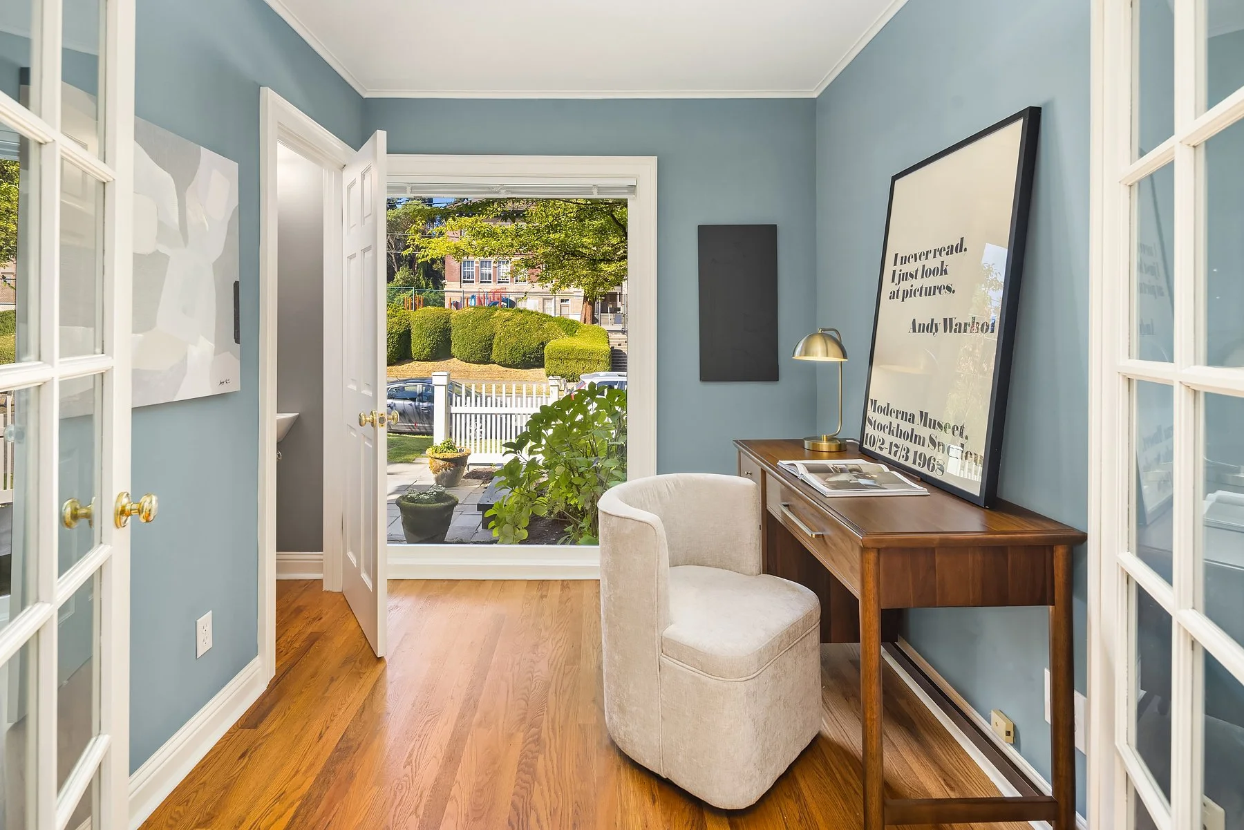 Home office in a Seattle home with soft blue walls, a wood desk, a cream swivel chair and a garden view