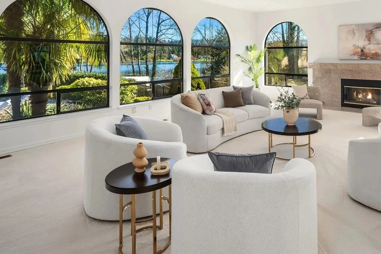 Staged living room with arched windows overlooking a lake, a curved white sofa and boucle swivel chairs