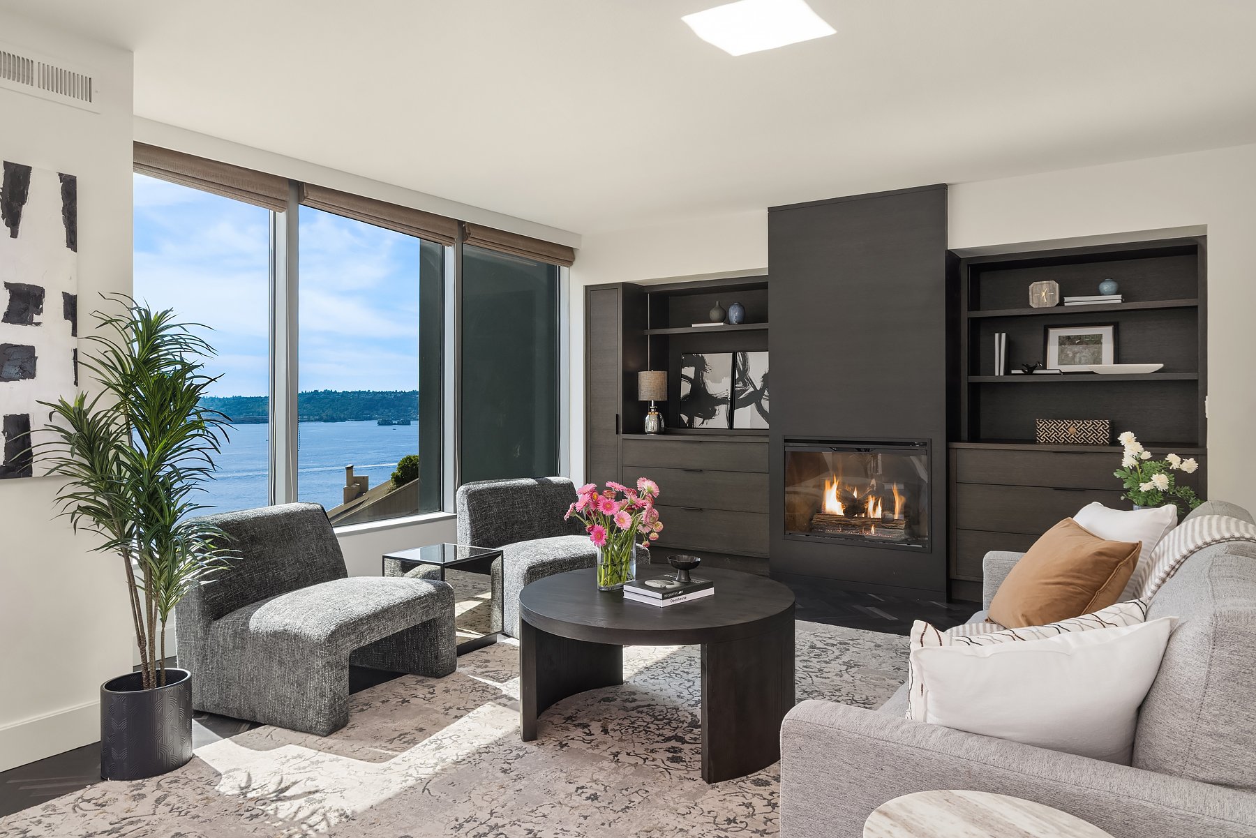 Staged downtown Seattle condo living room with water views, a fireplace and gray lounge chairs