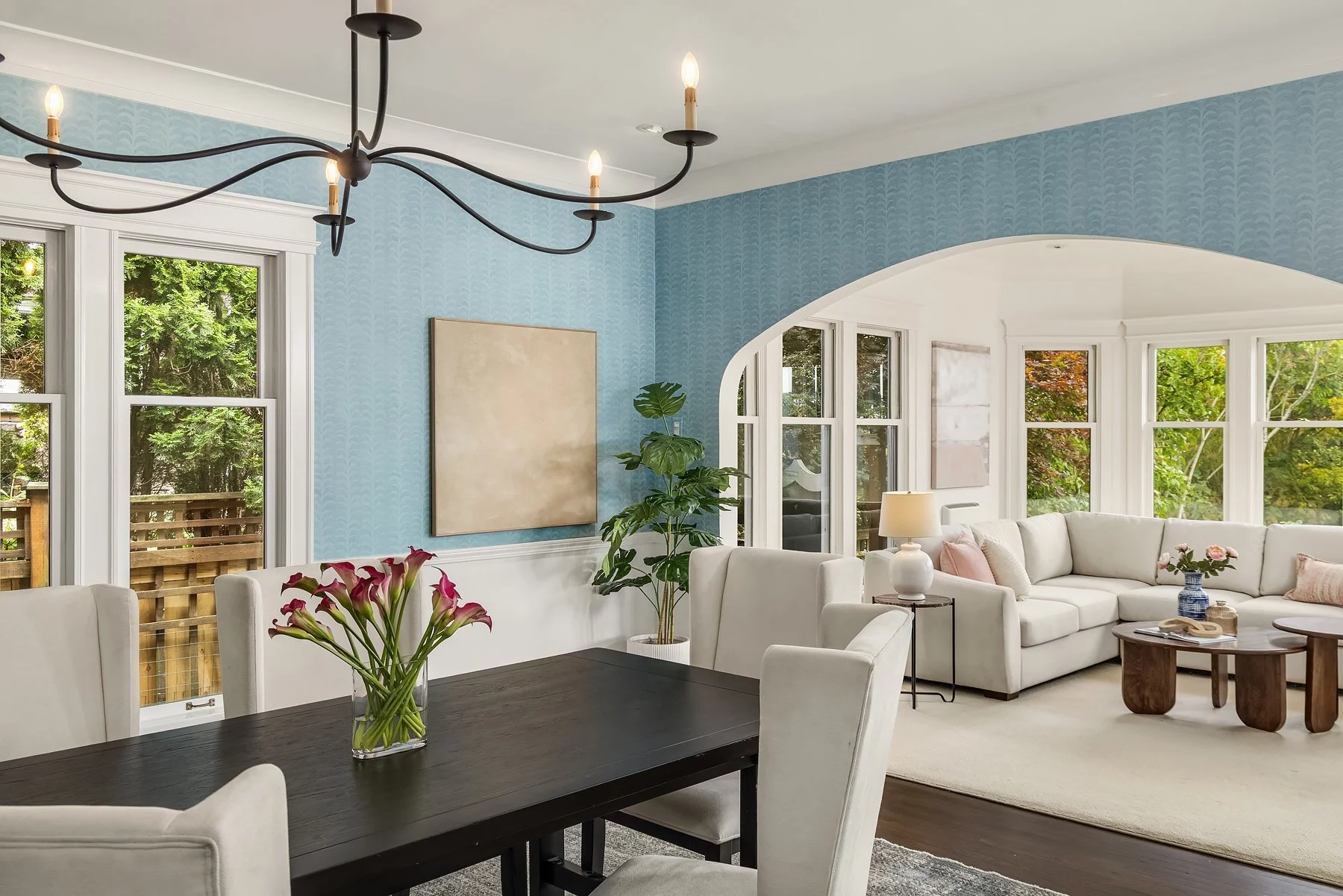 Staged dining room with iron chandelier and arched opening to the living room in a Seattle home