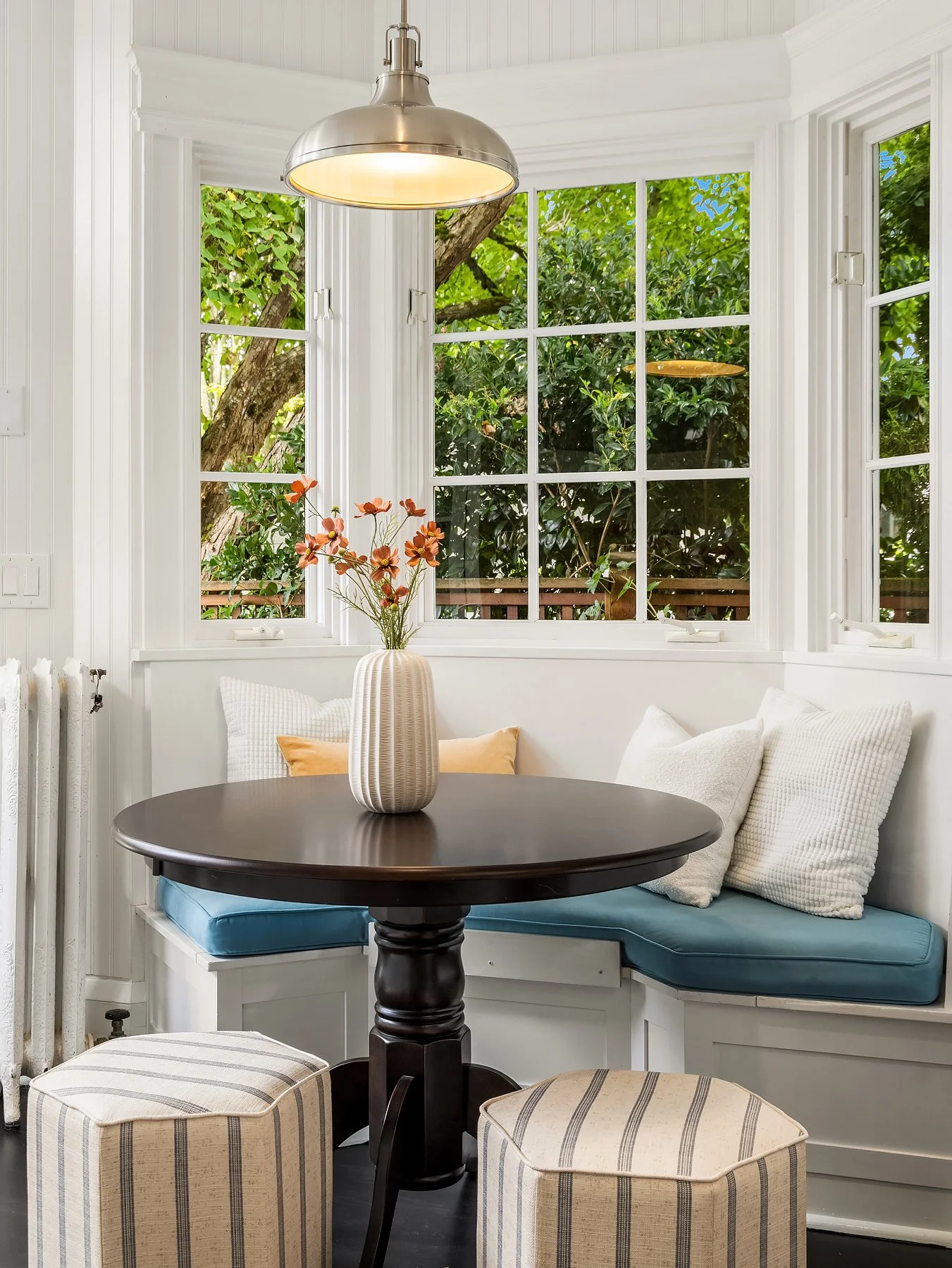Breakfast nook staged with a round pedestal table, blue bench cushions and striped ottomans