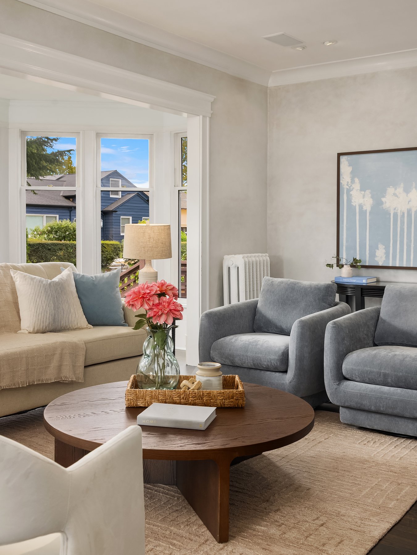 Staged living room with gray armchairs, a cream sofa and a round wood coffee table in a Seattle home