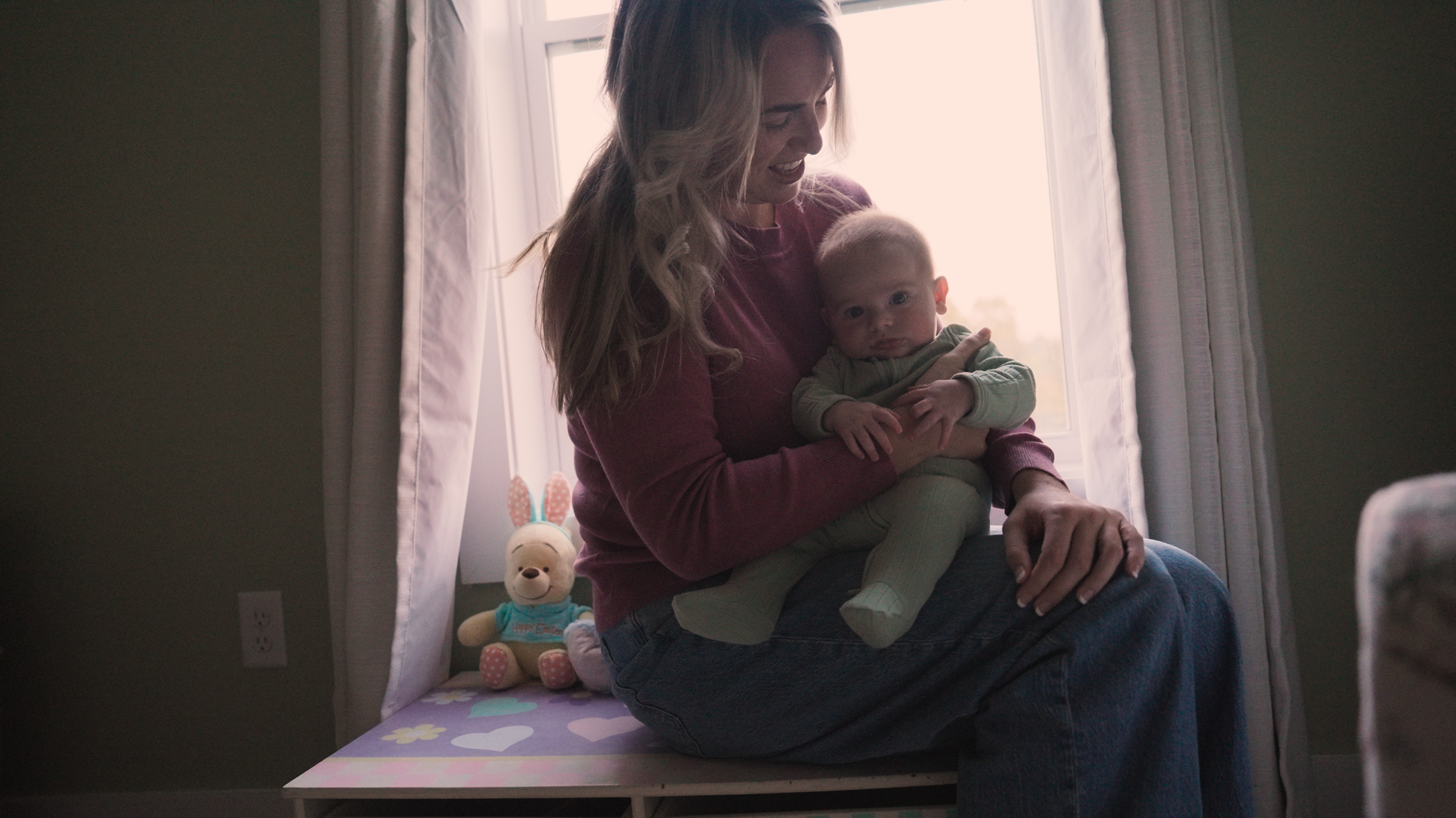 Mother sitting by a window holding her 3-month-old baby in soft silhouette — intimate newborn motherhood film by Tara O’Brien Family Films in Louisville, Kentucky.