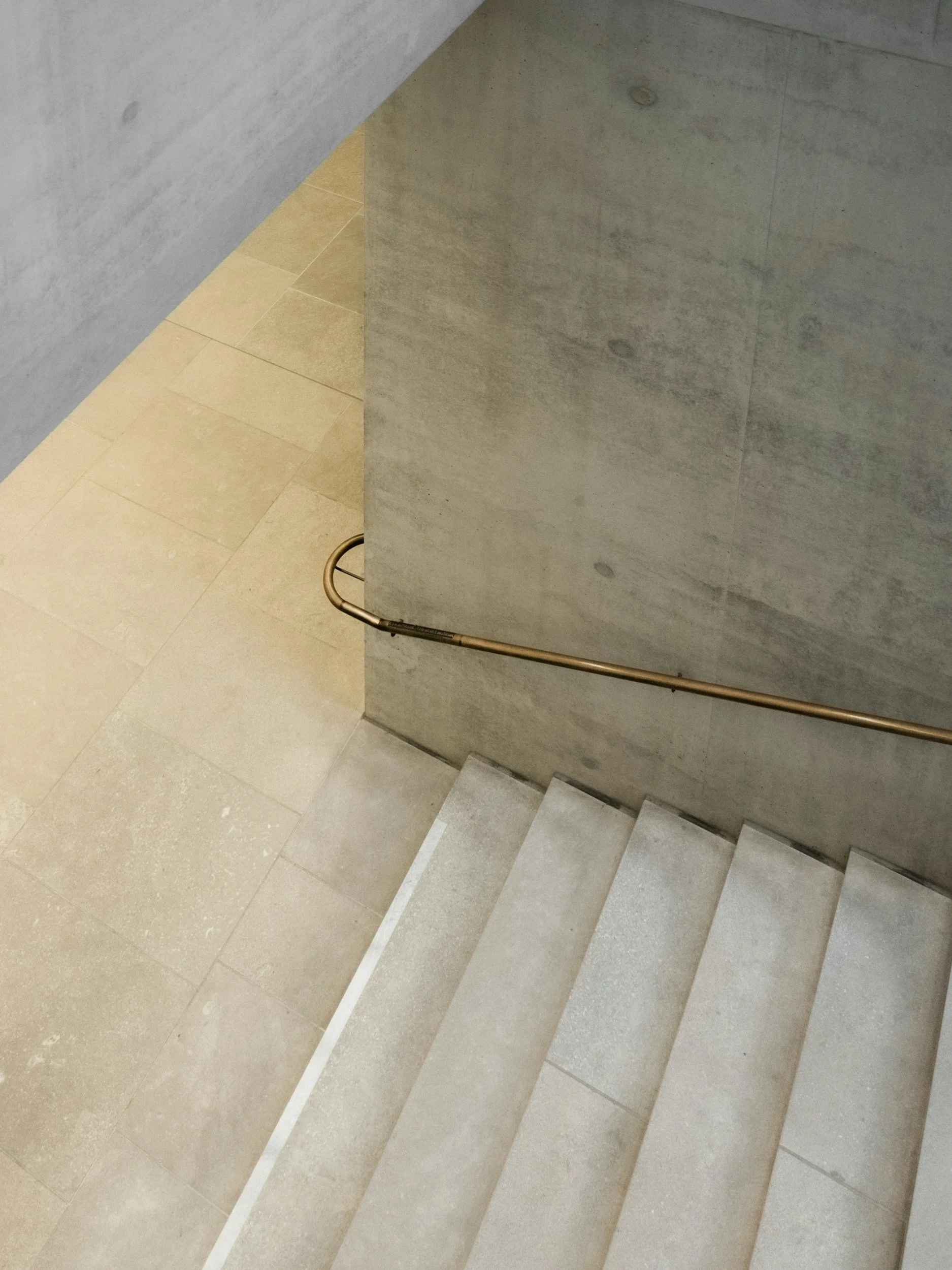 A top-down view of a staircase with light-colored steps, a concrete wall on the side, and a metal handrail.