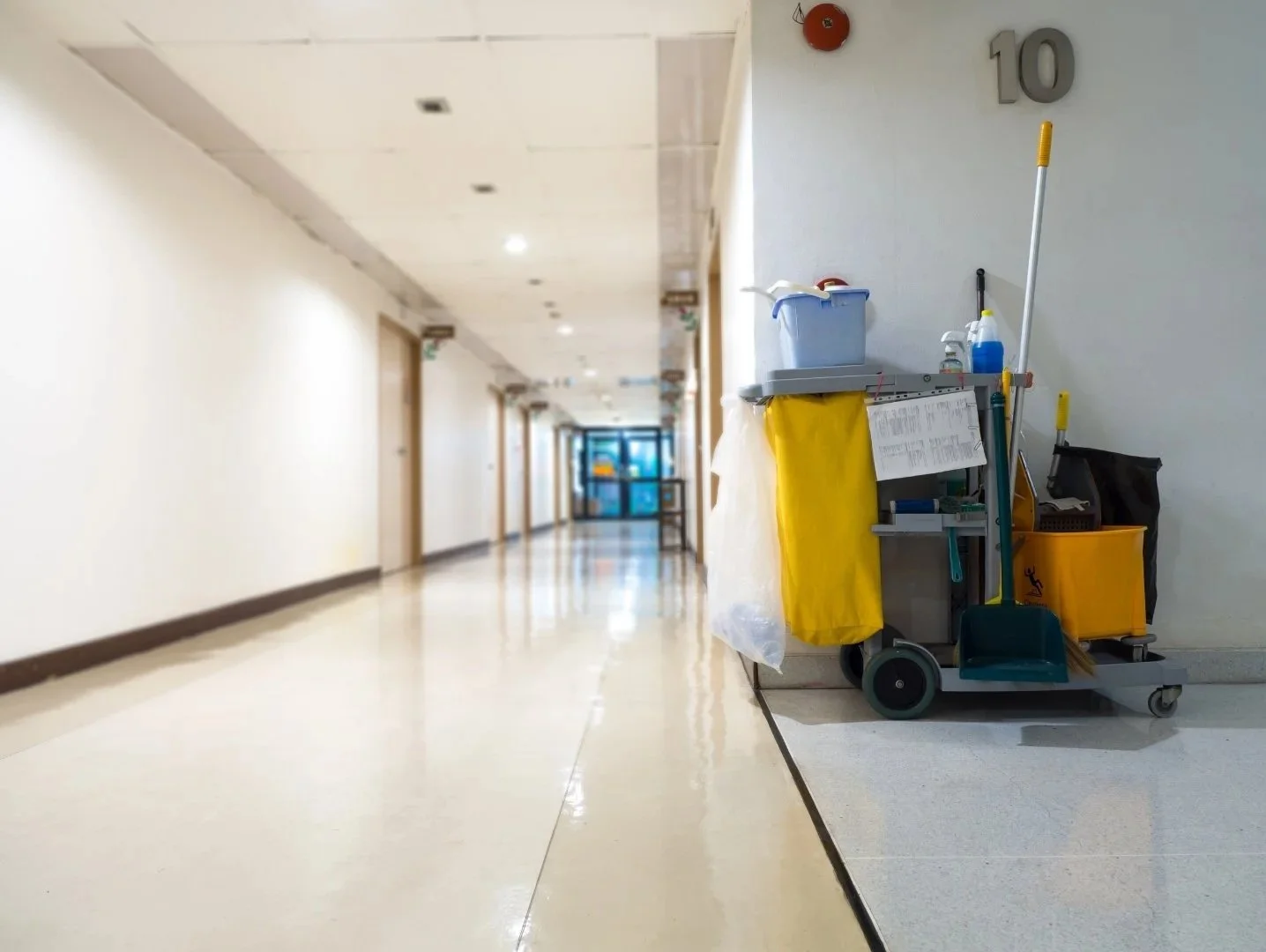 Empty hallway in a building with cleaning cart against the wall on the right side.