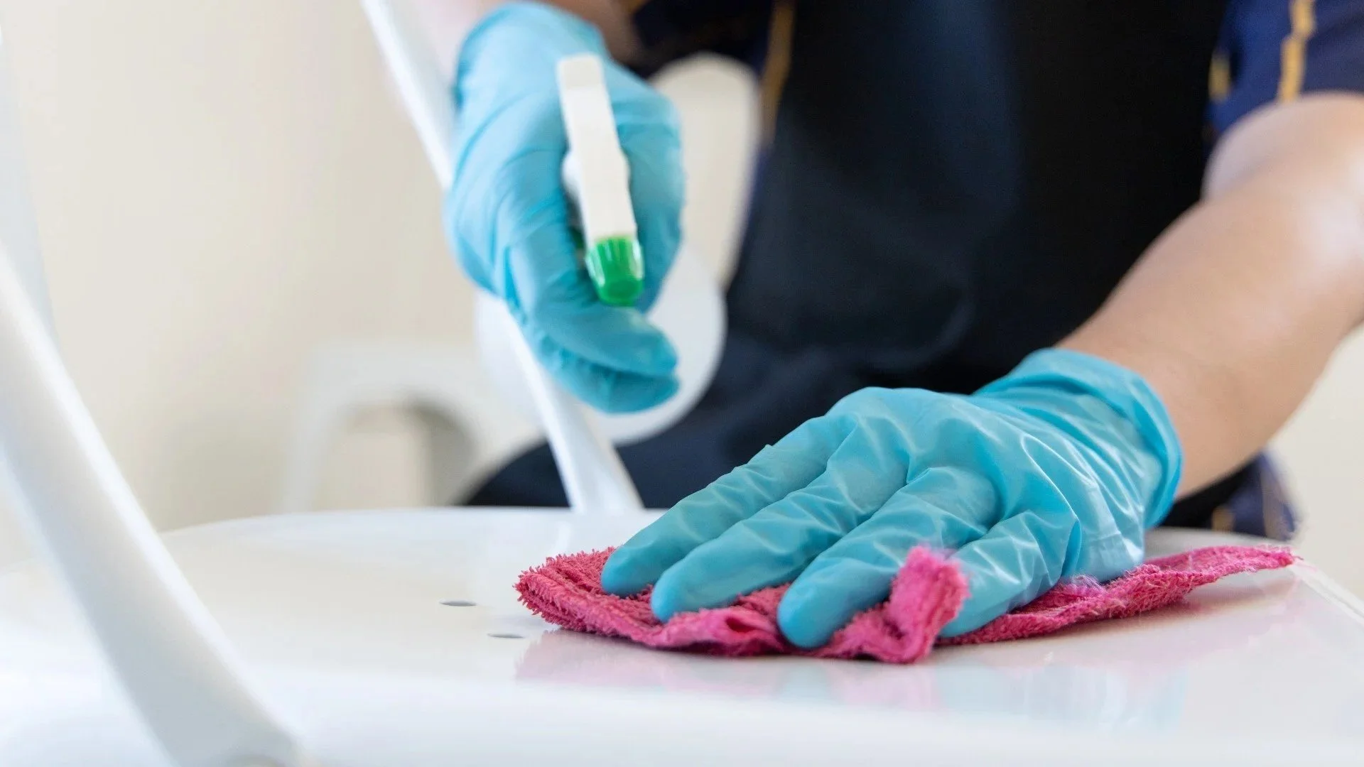Person wearing blue gloves cleaning a white surface with a pink cloth, using a green-capped swab or test tube in a medical or clinical setting.