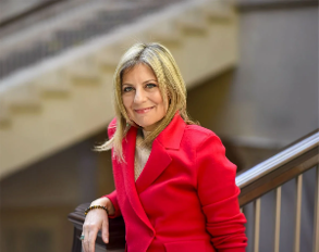 Danielle, a woman in a red business suit leaning on a stair rail.