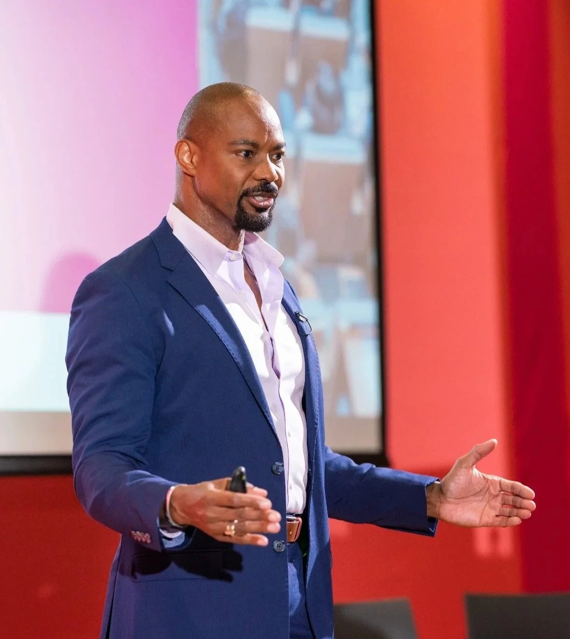 A man, Thomas Barnette, giving a presentation in a conference room with a red wall and projection screen.