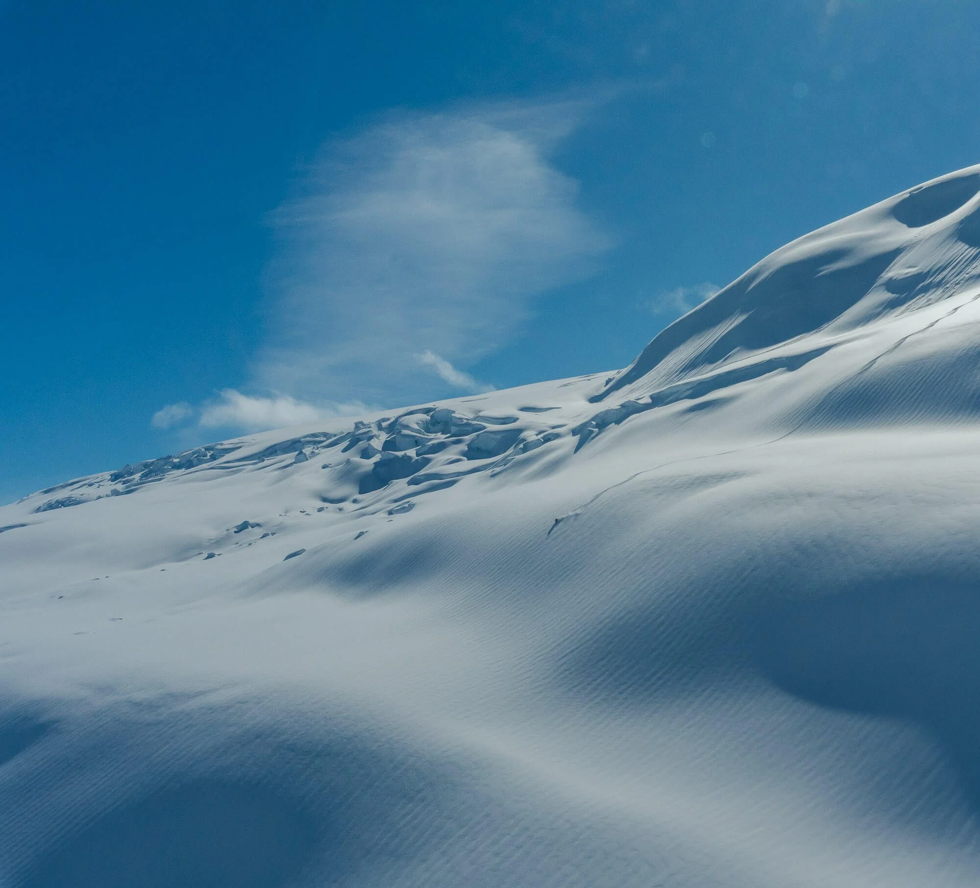 Snow-covered mountain with blue sky and sparse clouds.