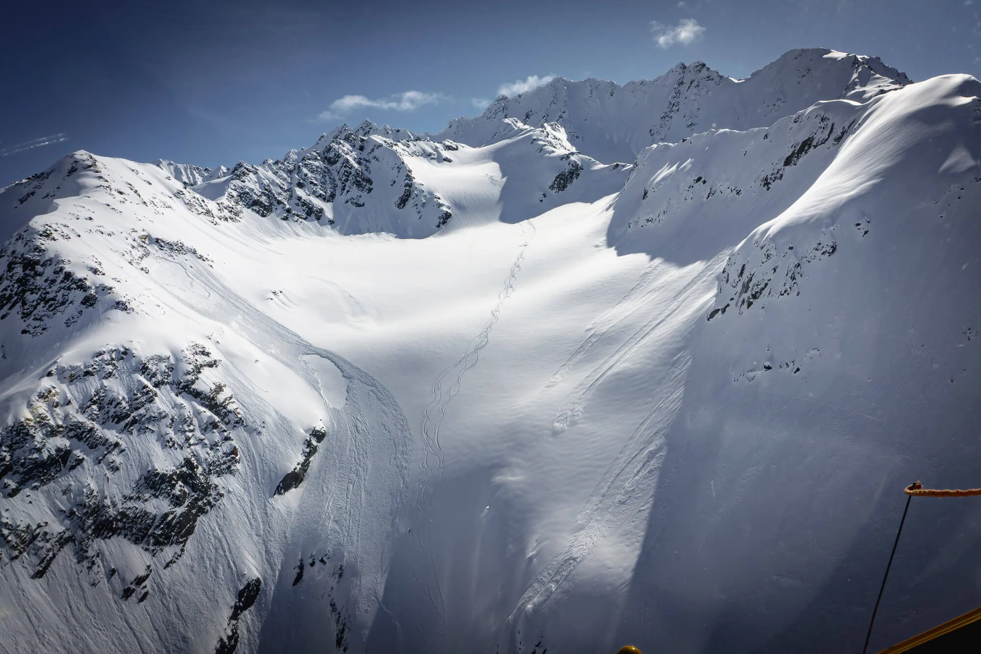 Snow-covered mountain range with ski tracks in the snow and a blue sky with clouds.