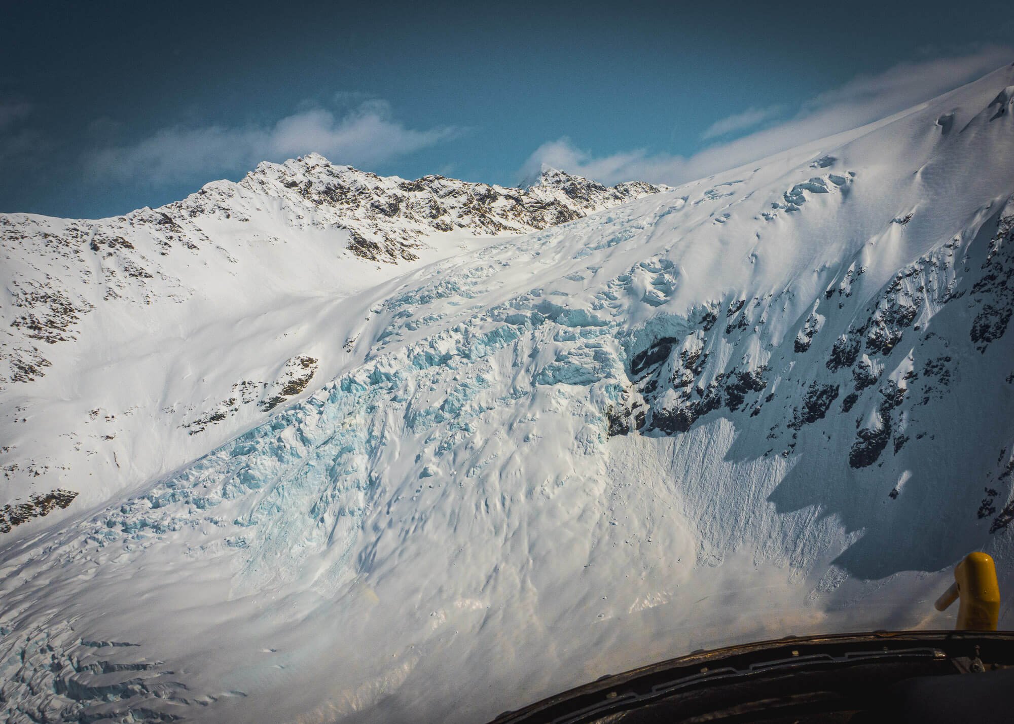 Snow-covered mountain landscape with a glacier and rocky peaks under a blue sky, taken from a vehicle's perspective.