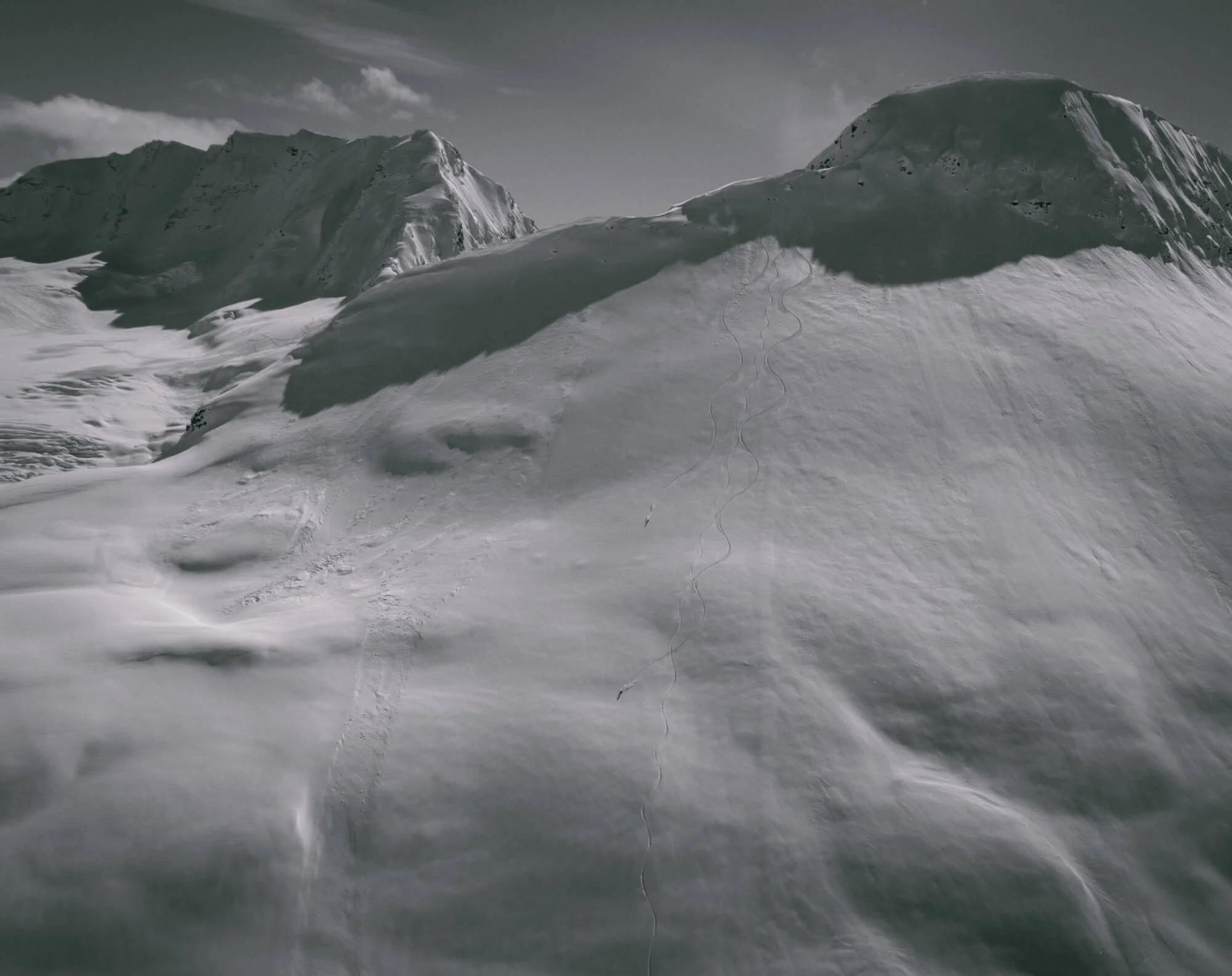 Snow-covered mountain landscape with tracks in the snow and two prominent peaks in the background.