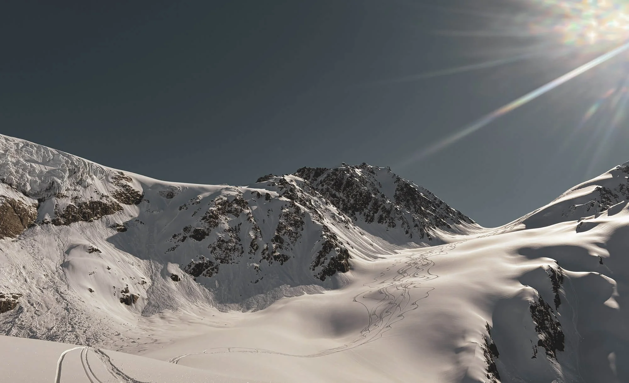 Snow-covered mountain landscape under a clear blue sky with the sun shining.