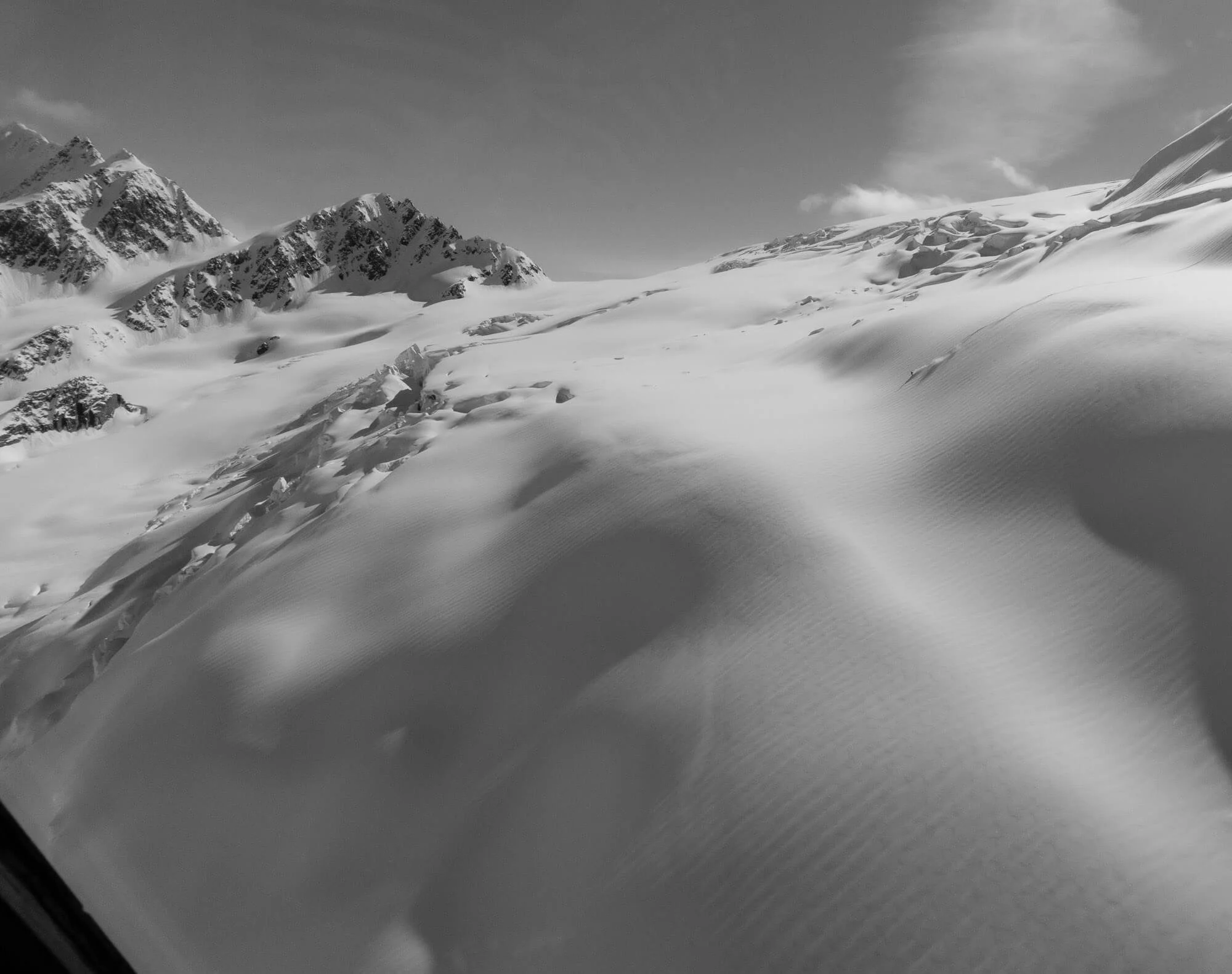 Snow-covered mountainous landscape with tracks in the snow and a cloudy sky.
