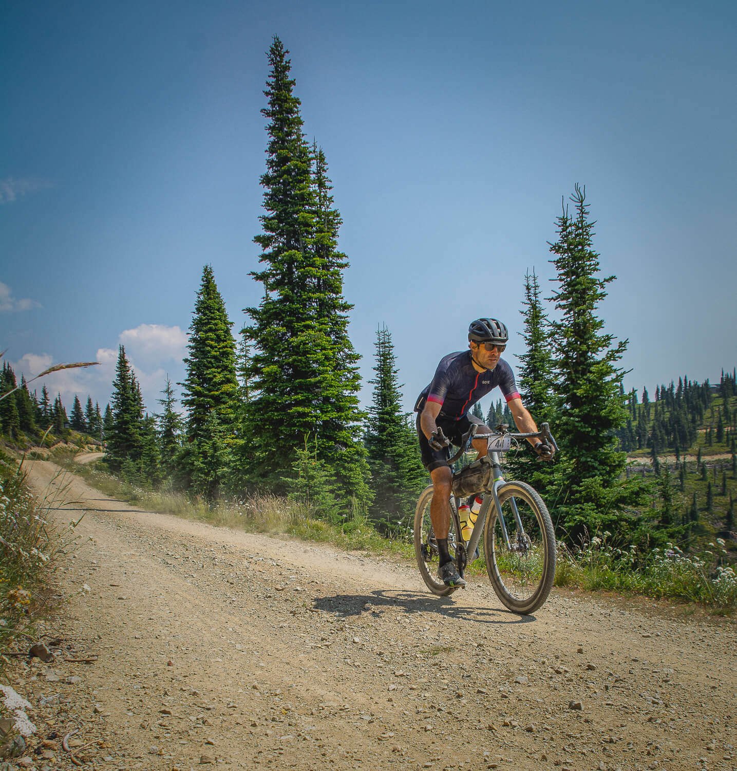 A male cyclist riding a mountain bike on a dirt trail in a forested area during daytime.