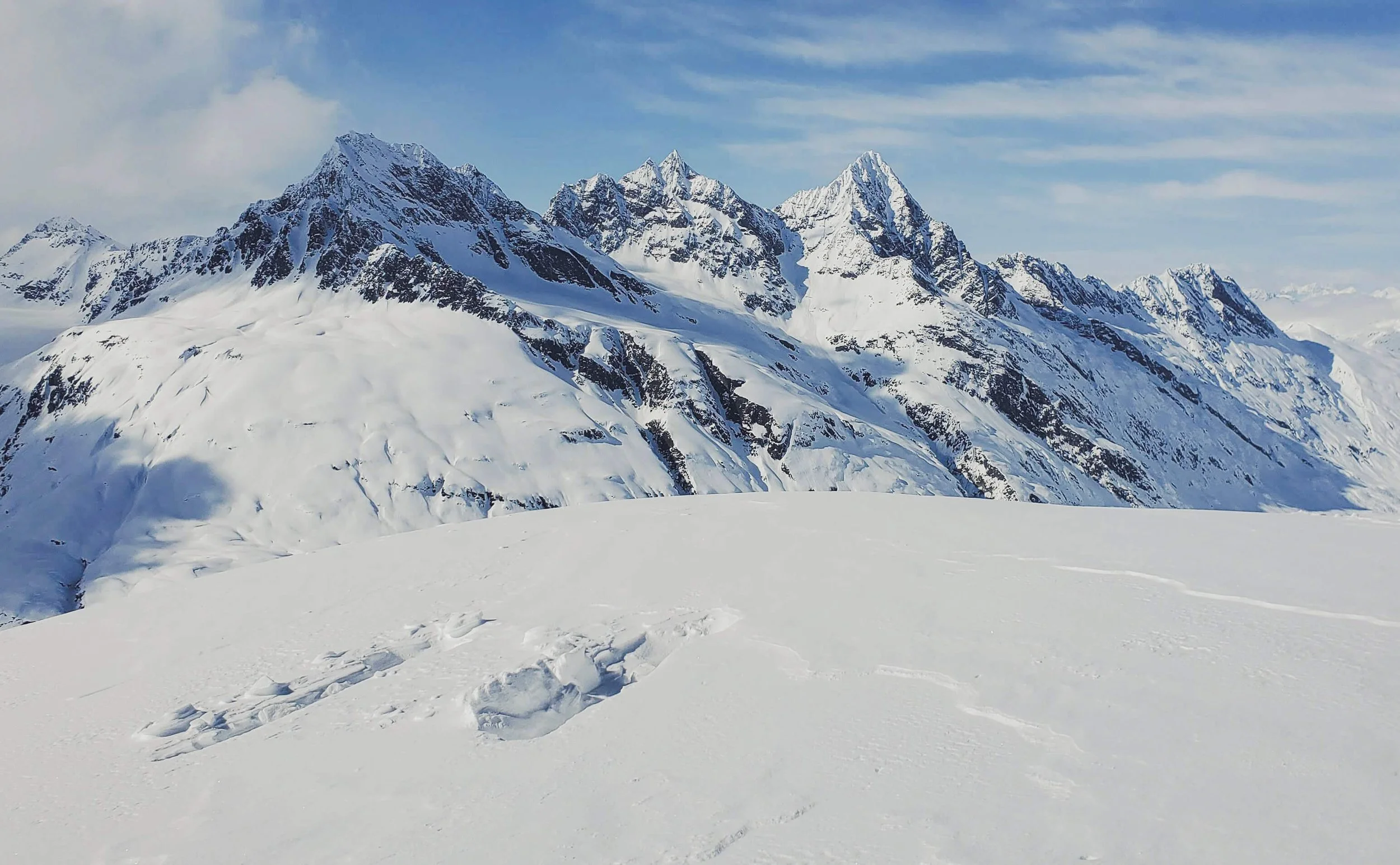 Snow-covered mountain range with sharp peaks under a blue sky with scattered clouds