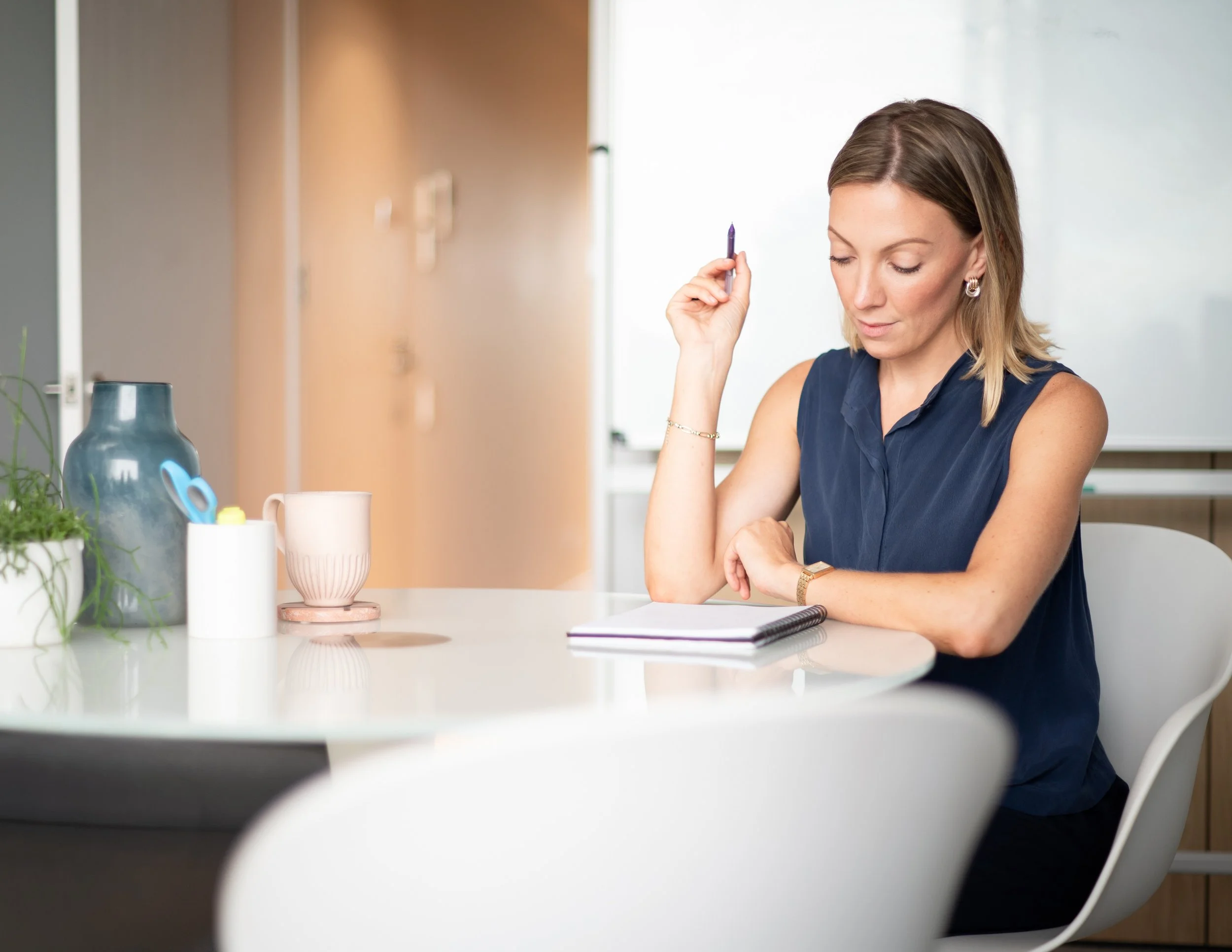 Manager completing a personality profile as part of a coaching session, sitting at a white table with a notebook and pen, in an office or conference room setting.