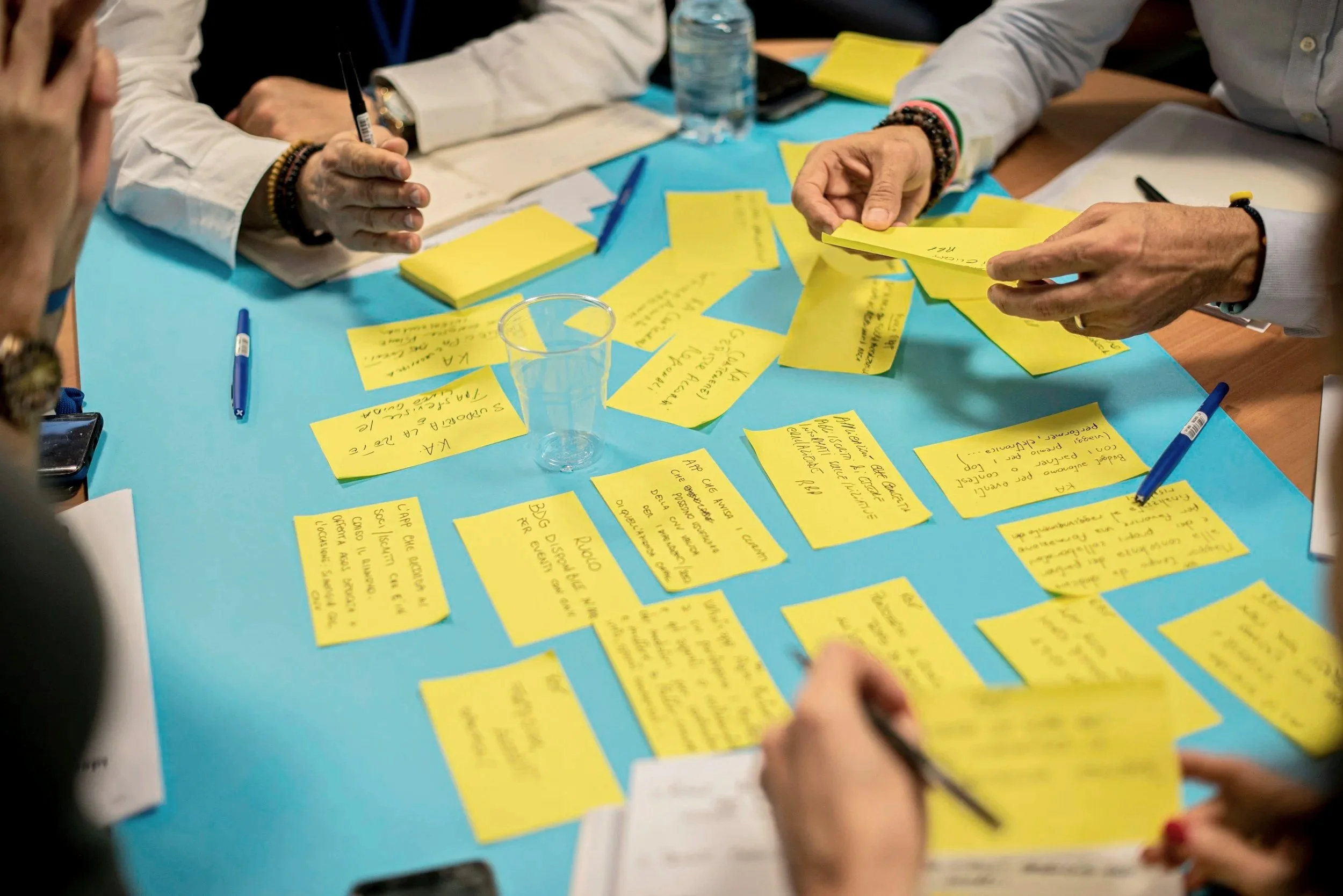 People working on a brainstorming session with yellow sticky notes on a blue table, writing and discussing ideas.