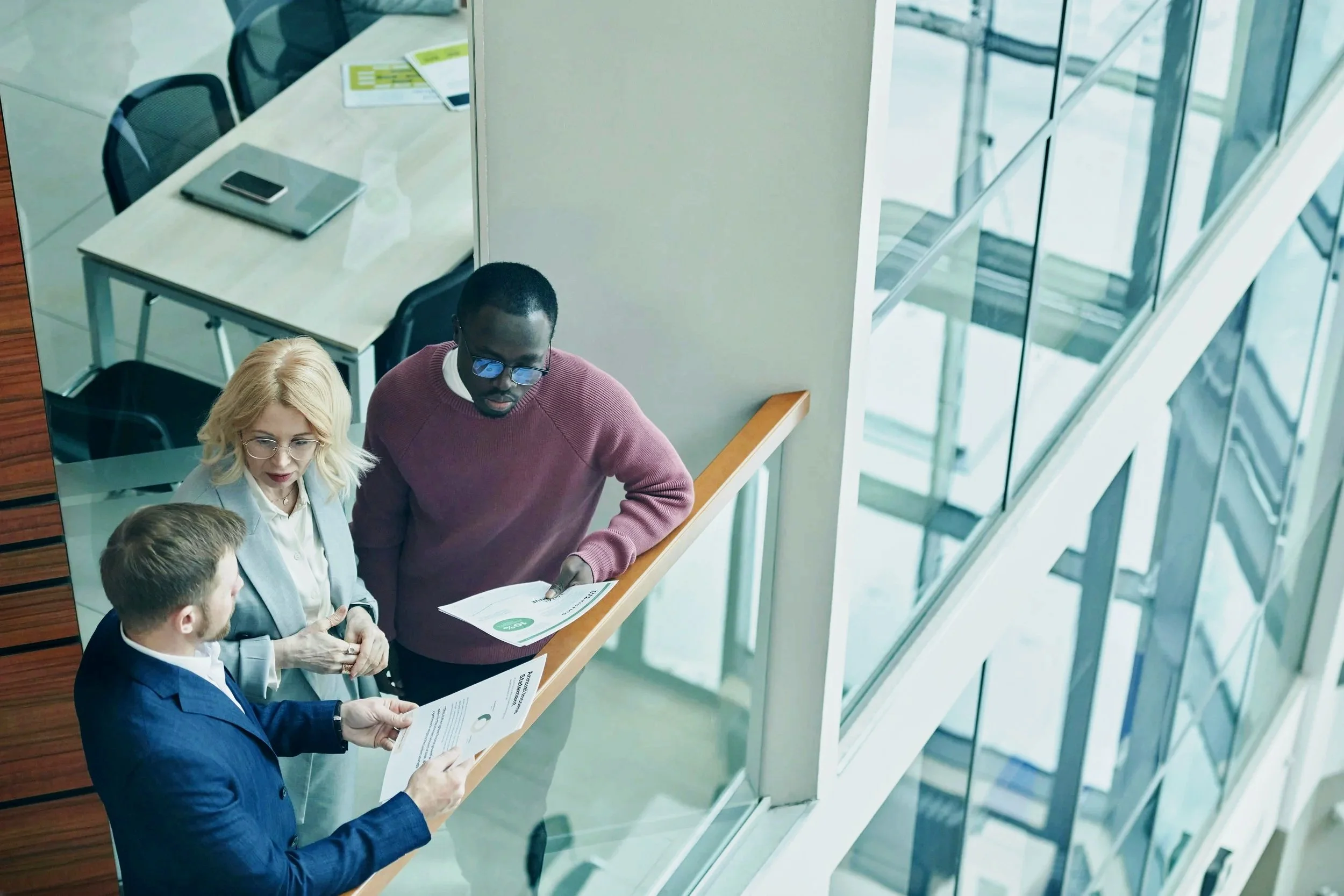 Three people in a business meeting discussing documents in a corporate office setting. The three people are from a variety of levels across the organisation.