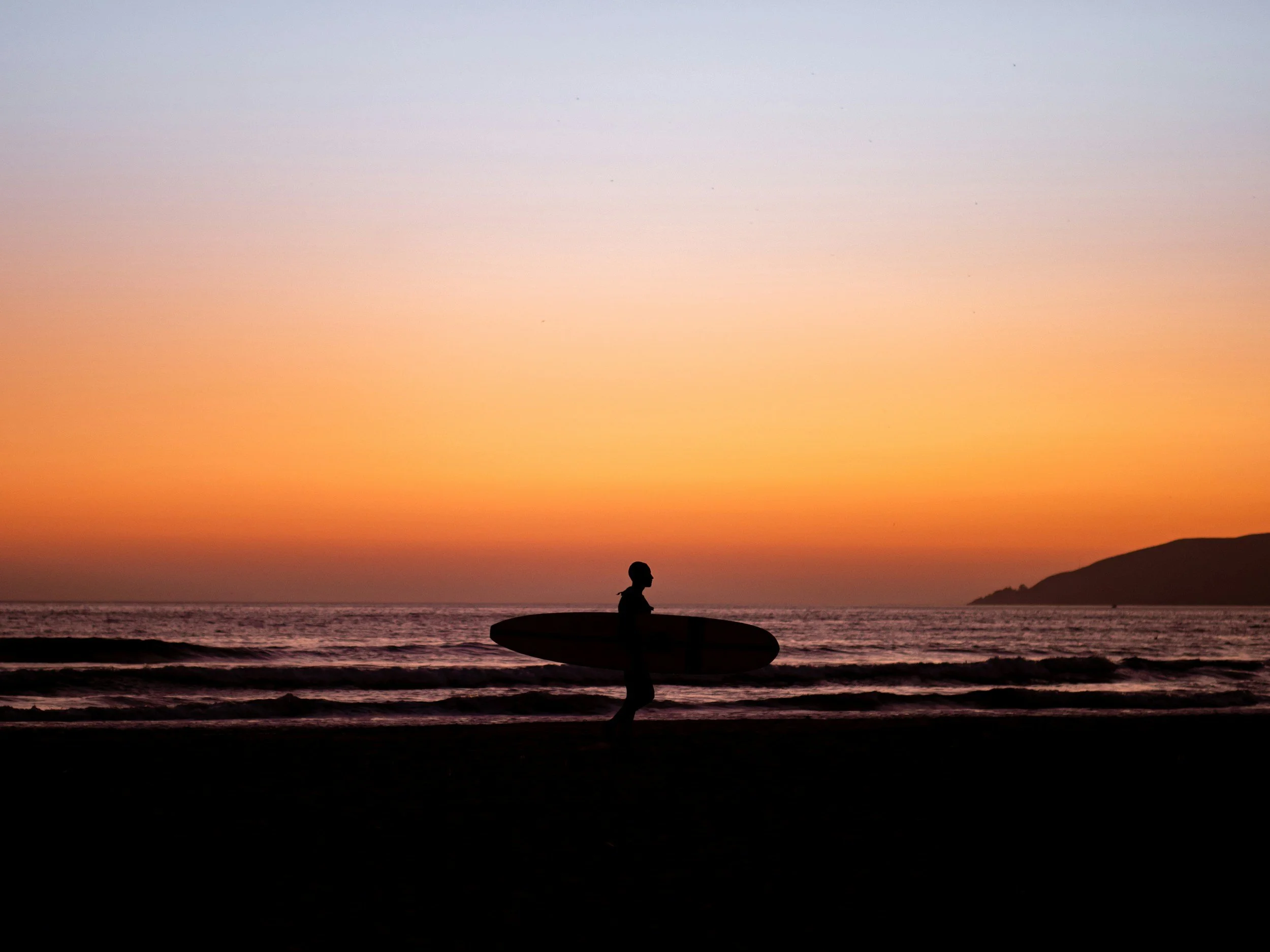 Surfer walking on the beach during sunset in central coast, California. 