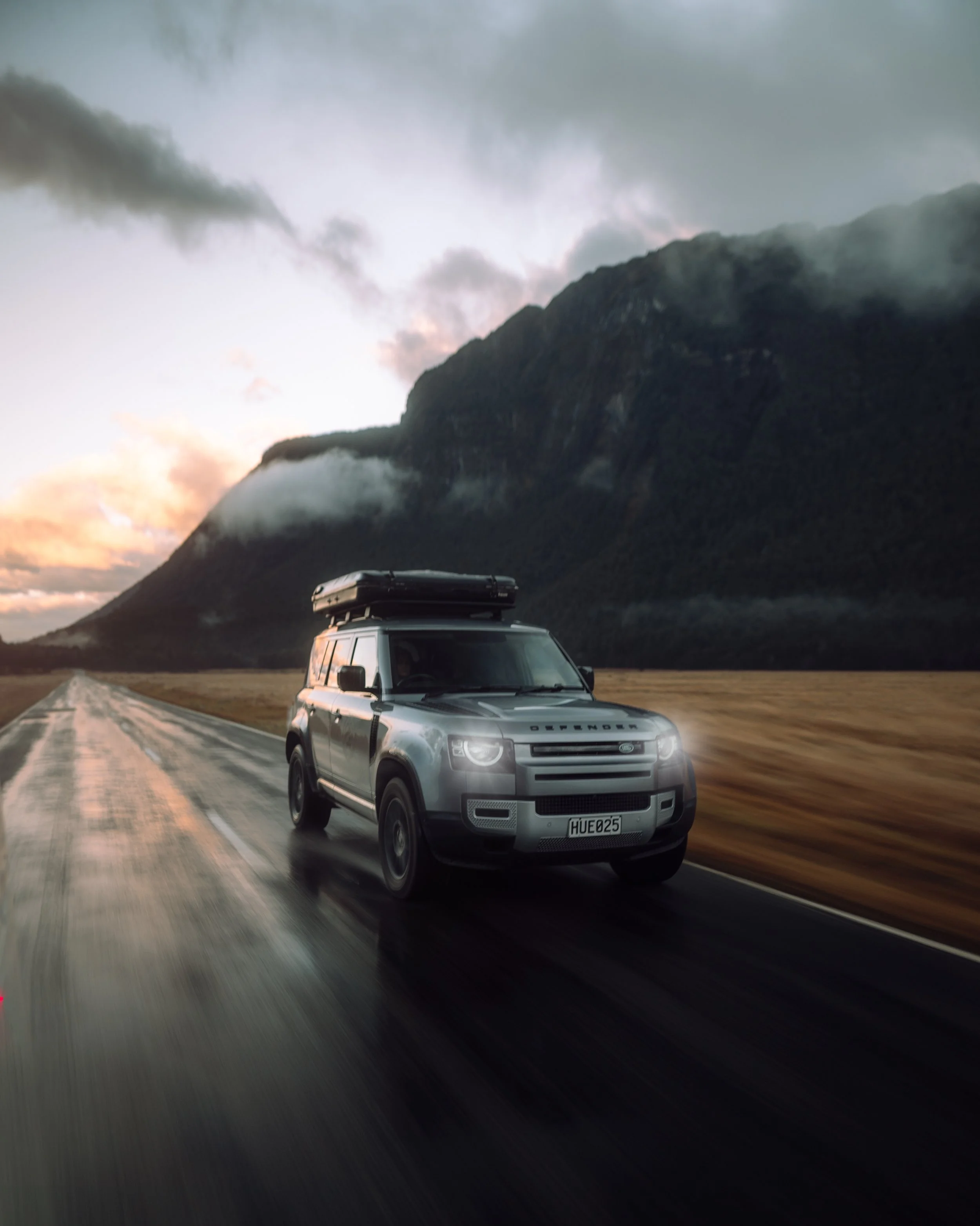 Land Rover Defender driving New Zealand alpine highway at sunrise