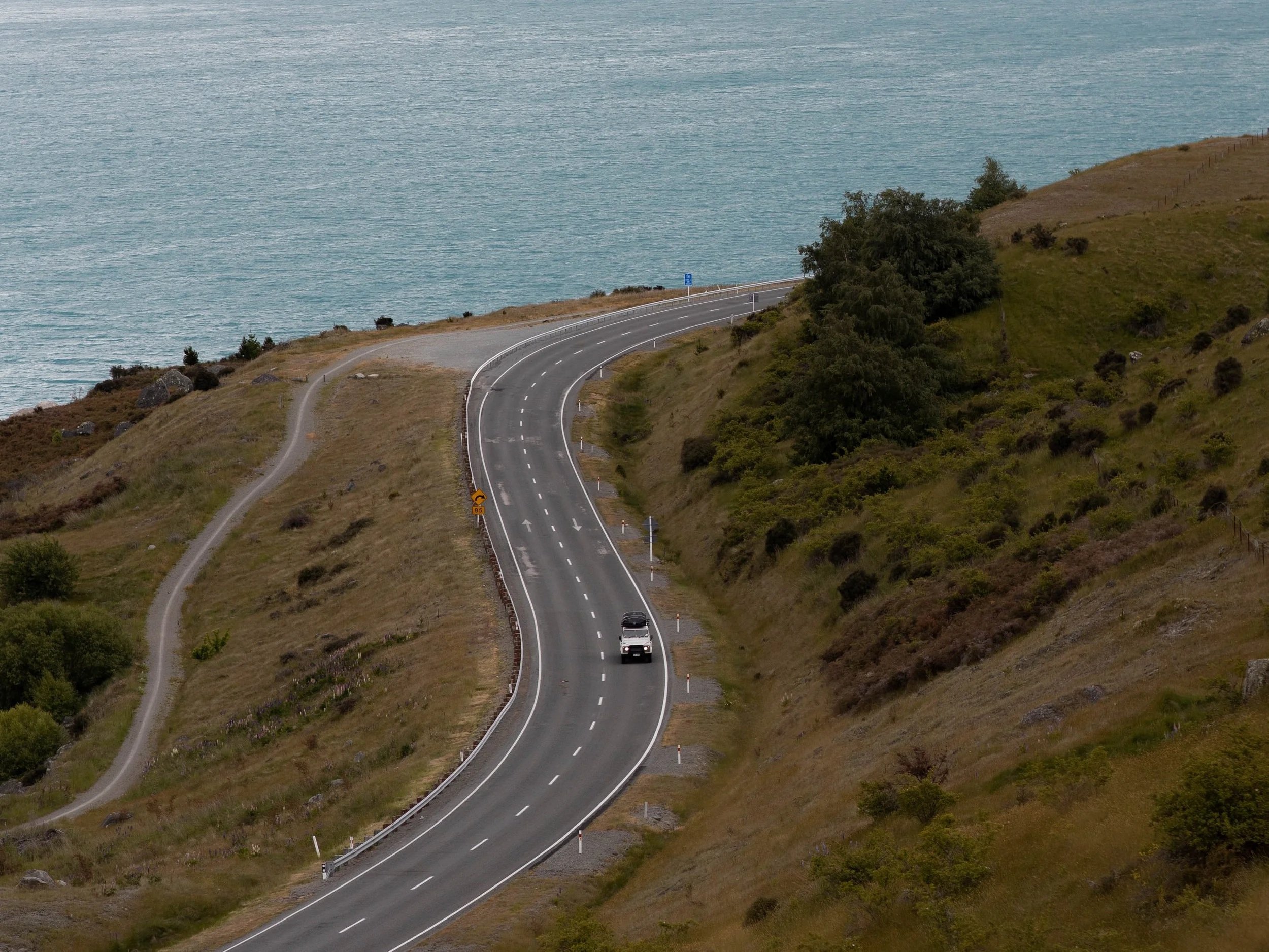 Car on winding coastal highway in New Zealand – scenic self-drive road trip