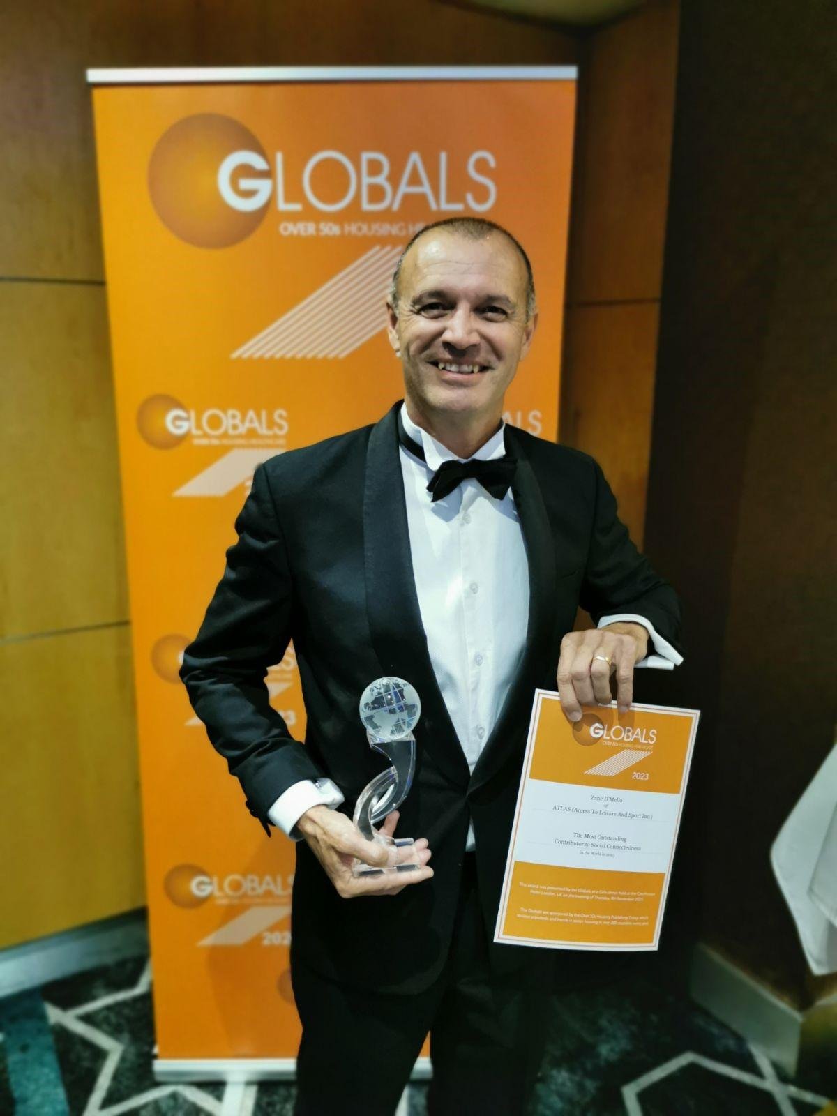Zane D'Mello in a tuxedo holding an award and a certificate at an awards event.