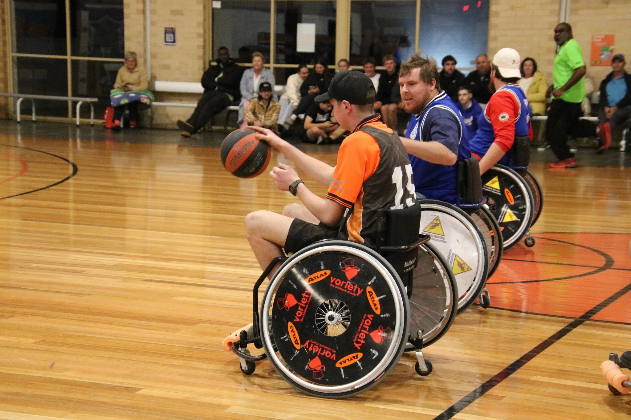 Wheelchair basketball game in progress with players and spectators in a gymnasium.