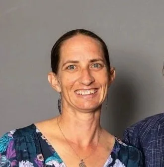 Marissa Drummond, smiling, wearing a floral top, against a neutral grey background.